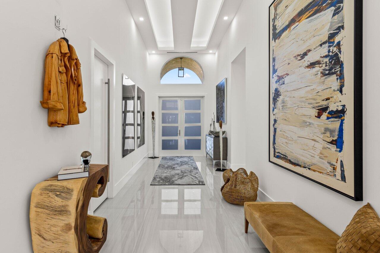 Step into a world of modern sophistication as you enter this exquisite one-story home, where thoughtful design and luxurious details create an atmosphere of refined comfort. The striking foyer, illuminated by contemporary lighting, sets the tone for the elegance and style that awaits. Beyond the entryway, a bright and inviting living room welcomes you with abundant natural light streaming through expansive windows. A standout feature of this space is the stunning large wine cooler, seamlessly blending style and function--perfect for entertaining or showcasing your collection. The heart of the home, the kitchen, is a masterpiece of modern design. Sleek and seamless cabinetry offers ample storage, while the expansive island provides plenty of seating for casual dining and social gatherings.