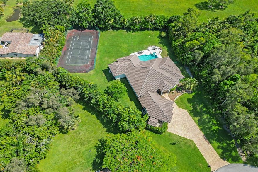 Welcome to the epitome of sophistication in Plantation Acres! This stunning estate is designed for luxury and comfort, featuring 5 bedrooms plus a home office, 5.5 bathrooms, split floor plan, home theater with seating for 12 & a chef's kitchen. Set on a vast 49,077 square foot lot, the property boasts a North/South facing tennis court, below ground pool w/jacuzzi & an outdoor shower. Enjoy alfresco dining with a built-in BBQ & refrigerator on your private patio, surrounded by a lush private yard. Indoors, revel in the tile and stone floors, an indoor wet bar & expansive living spaces tailored for entertaining. With a newer roof, hurricane shutters & ample parking in a tranquil cul-de-sac, this home offers a sophisticated lifestyle in a serene setting, ready for its next owner to cherish.