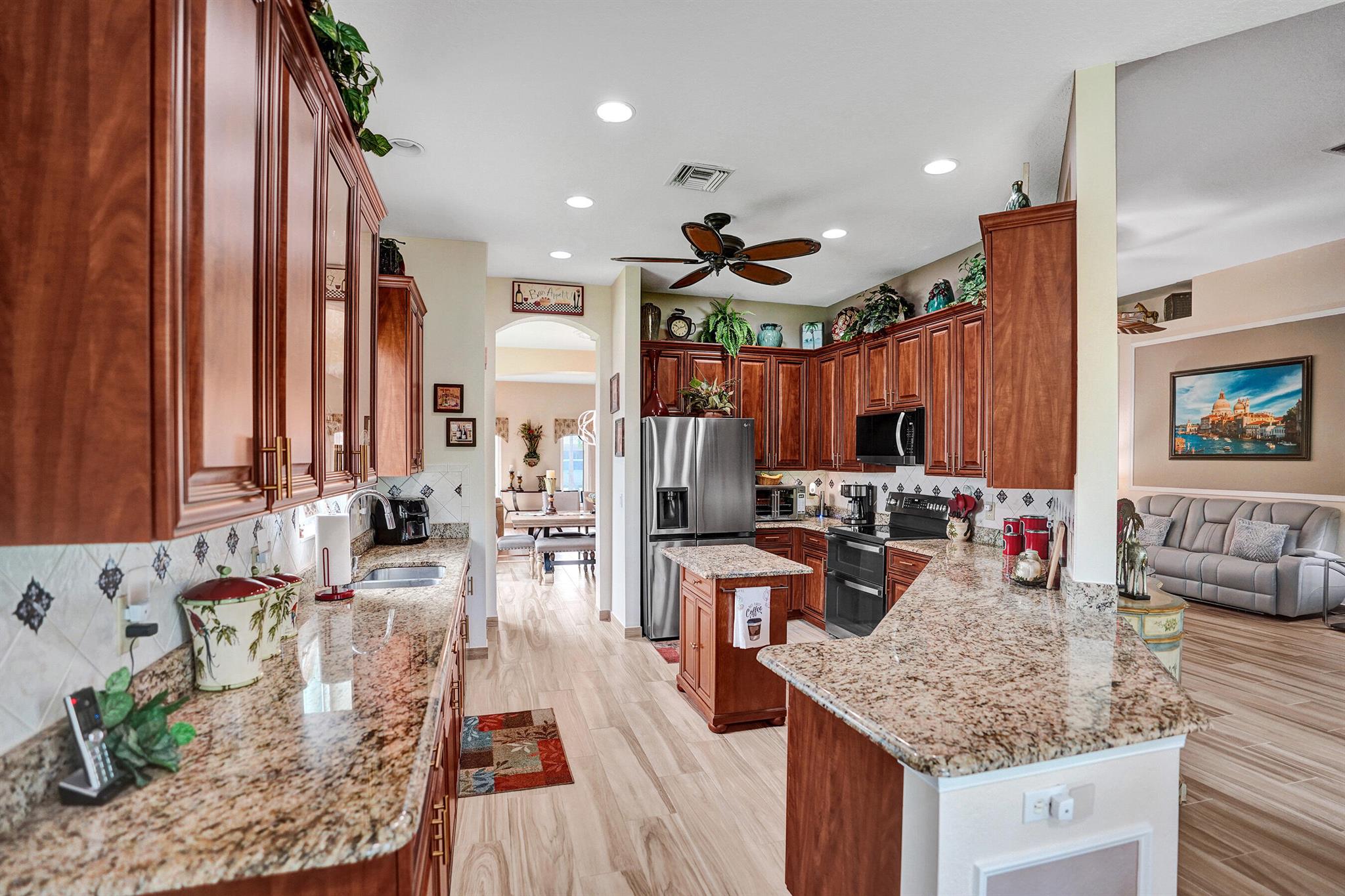 This 2BD/2BA + Den home is beautifully maintained and move-in ready. The main living areas feature elegant wood-look ceramic tile, and warm laminate flooring in the bedrooms. A spacious, light-filled layout includes a formal living room and separate dining area with arched entryways and decorator finishes.The kitchen boasts rich wood cabinetry, granite countertops, stainless steel appliances, and a convenient center island perfect for cooking and entertaining. The private primary suite includes generous closets and an oversized ensuite with dual vanities, a jetted soaking tub, and a step-in glass shower. Relax year-round in the large screened lanai, surrounded by lush landscaping and tranquil views. Additional features include hurricane-impact front door and windows,