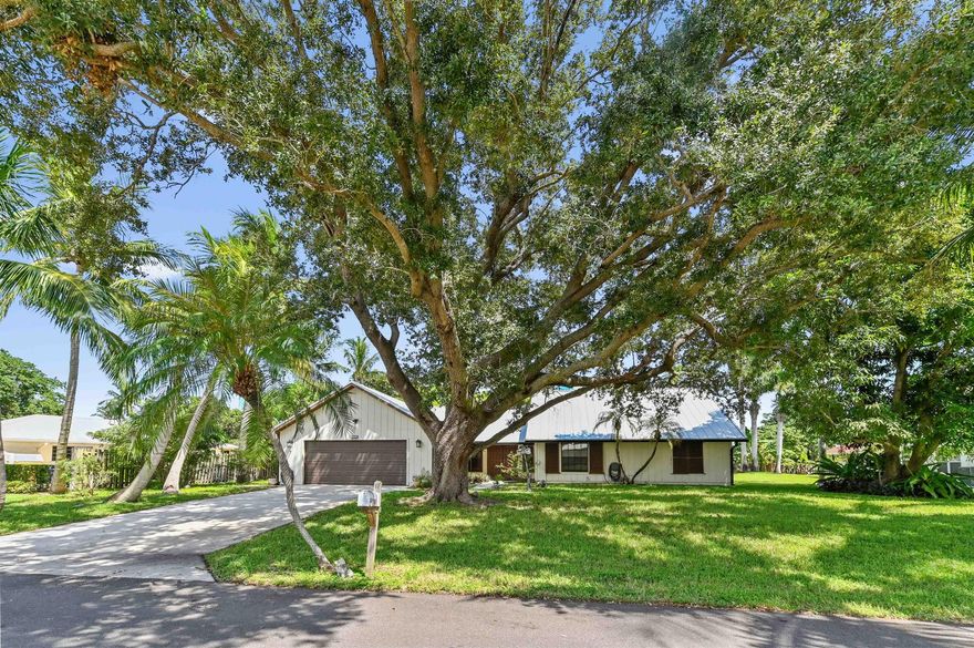 Welcome to this charming and beautiful 3 bedrooms and 2 bathrooms home, perfectly situated on a quiet desirable Hobe Sound community. The home offers immediate curb appeal, featuring a durable, modern NEW metal ROOF and a lush, tropical setting with mature shade trees and palms. Step through the handsome double entry doors into a welcoming interior defined by an open floor plan and bright tile flooring. The living room is a true centerpiece, boasting a dramatic, high vaulted ceiling with exposed wood beams and a cozy built-in area, creating a warm and expansive space for both relaxation and entertaining.