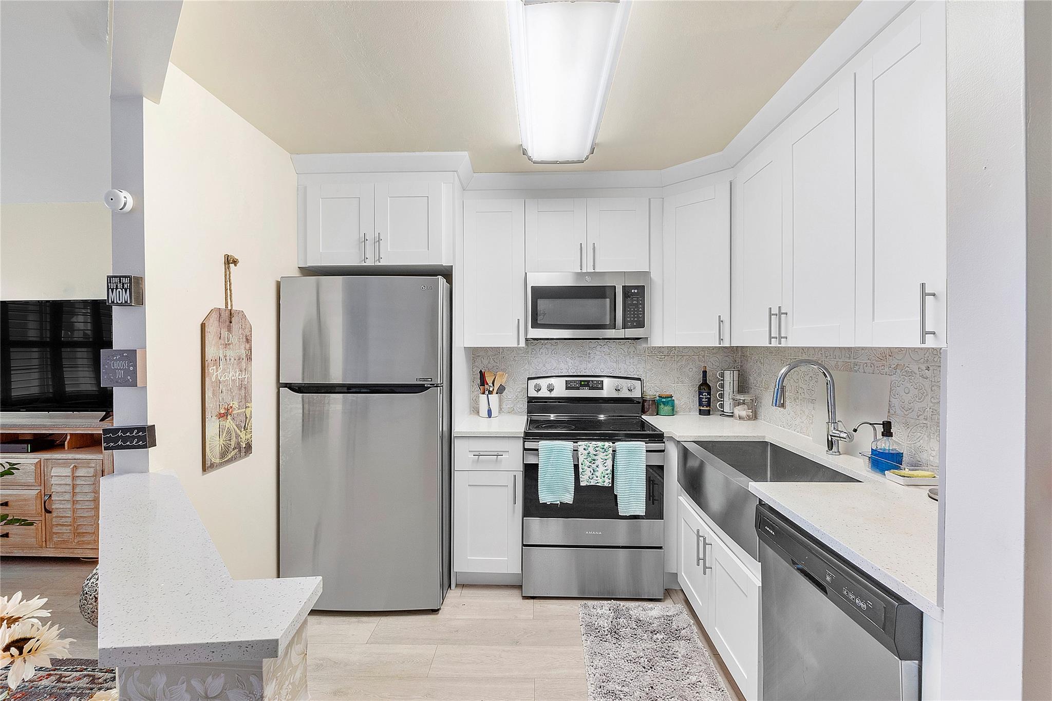 FIRST FLOOR. UPDATED UNIT with gorgeous gray wood tile floors seamlessly flowing throughout. The heart of this home features stunning granite countertops complemented by crisp white shaker cabinets and sleek stainless steel appliances, including a stylish farmhouse sink. Enjoy the efficiency of a tankless water heater and the soft ambiance provided by white plantation shutters. The updated bathroom boasts a chic vanity with a frameless shower door for a touch of luxury. Step outside to your private outdoor patio accessible from the bedroom, perfect for morning coffee or evening relaxation. This unit flawlessly blends style and comfort in a prime location. Don’t miss it!