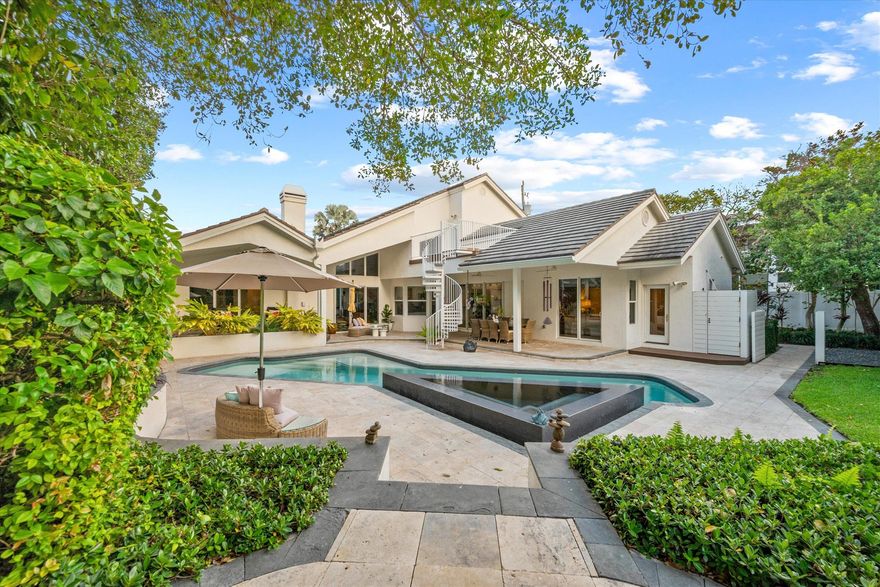 Exuding coastal sophistication, this lushly landscaped four-bedroom estate in prestigious Ocean Ridge combines modern elegance with timeless design. Dramatic vaulted ceilings, polished Saturnia floors, and a striking stone-mantel fireplace highlight the open living spaces, while walls of glass invite natural light and garden views. The expansive yard, surrounded by tropical landscaping with recent upgrades, creates a private oasis. Just three blocks from the beach, this storm-secure home features hurricane-impact windows and a generator, epitomizing refined coastal living.