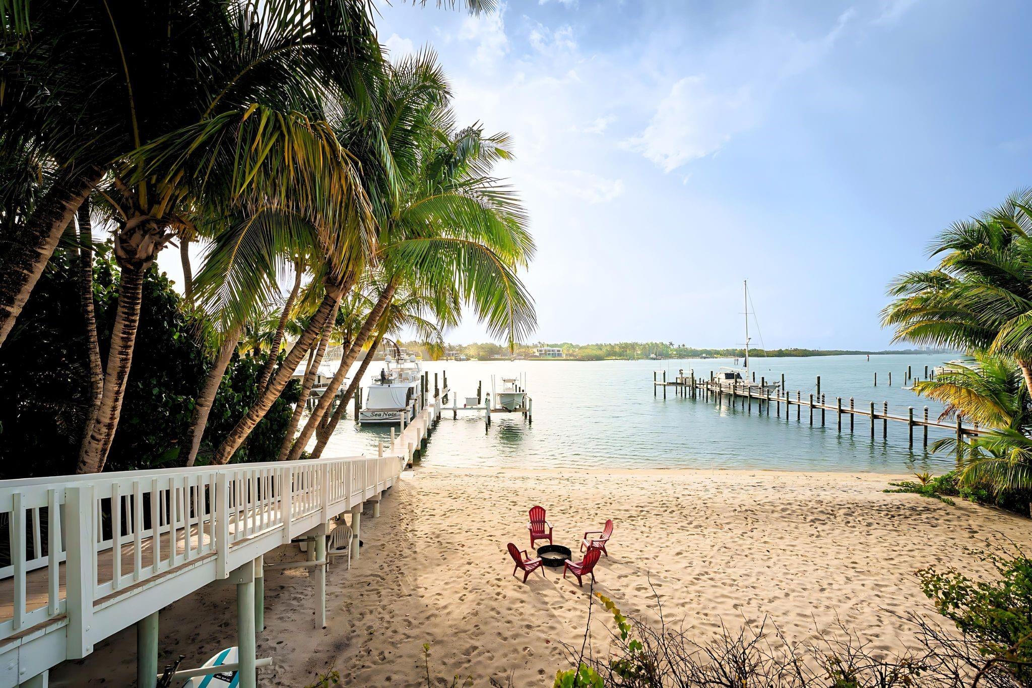 A true waterfront gem with its own PRIVATE BEACH! In one of Florida’s most prestigious neighborhoods, this estate offers 100+ feet of Intracoastal frontage in a no-wake zone with dockage for an 80-ft yacht, boat lift & 3 wet slips. Enjoy sunrises, sunsets & panoramic water views from nearly every room. The main house features 4 beds, 3.5 baths, a fully stocked chef’s kitchen with top-tier appliances, open living, ample storage & 2-car garage. The primary suite includes a boutique-style walk-in closet & resort-style microbubble tub. Outdoors: heated pool, multi-level decks, tropical gardens w/ orchids & sitting areas. A separate guest house for added privacy & charm. Fully furnished, turnkey, w/ Sonos & Wi-Fi. Weekly maid, pool & landscaping services included—your personal paradise awaits!