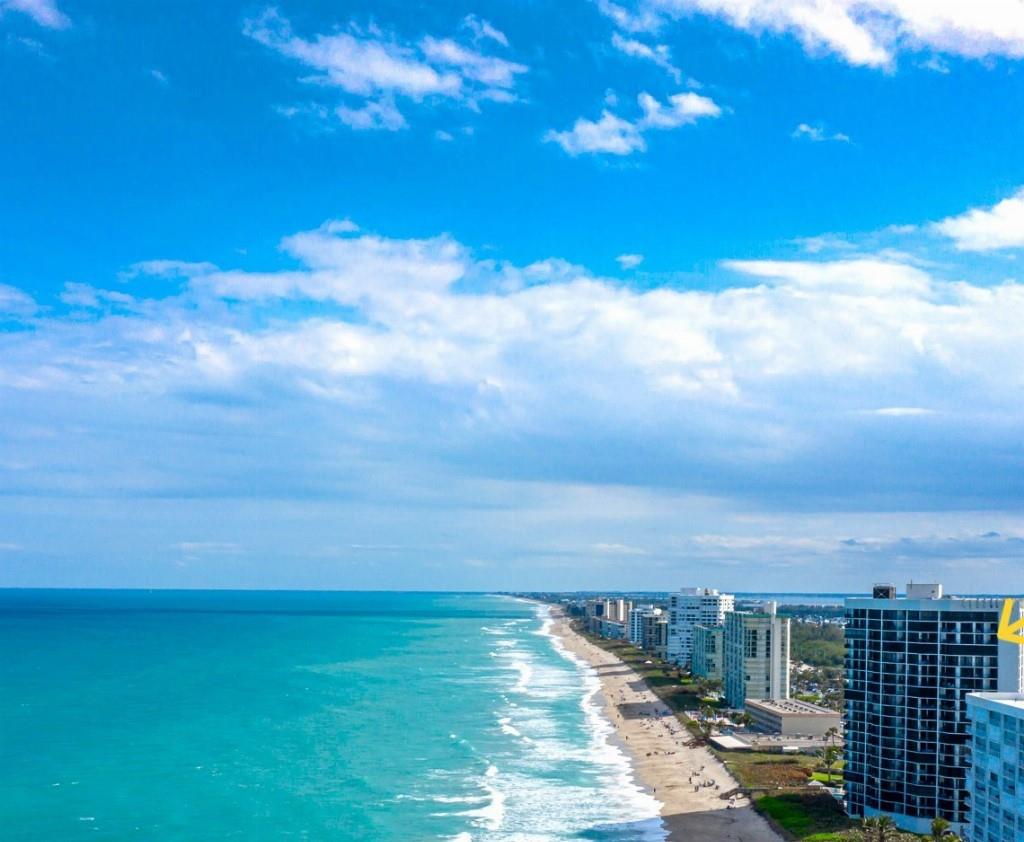 Panoramic water views from every room, 19th floor end unit, beautifully renovated.
Ocean views from Dining, Kitchen, Living, Master bedroom. Enjoy wraparound balconies from LR to Master bedroom. Sunset views of the Indian River from West side Master BR & Guest rooms.
Entry Foyer with a lounge chair & console table, provides counter for in or outgoing mail, & beach towel storage.
Large kitchen for cooking & entertainment, granite counters, travertine back splash with neutral cabinets. Bar stool serving area, stainless appliances new M/W, & separate large pantry. The sweeping views of the Atlantic Ocean from the kitchen are stunning! The corner end unit doesn’t feel like a typical condo box, as natural light flows through the condo all day.