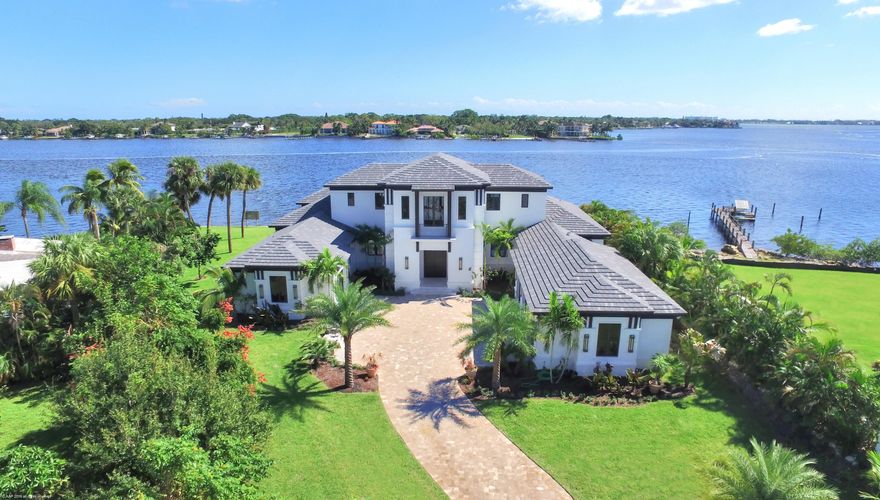This beautiful, contemporary British West Indies home built in 2016, is located on the widest part of the Loxahatchee River and is filled with modern flair and luxury finishes throughout. The 4 BR/4.5Bth/4-car garage home, with study/office and exercise rooms, is located on a quiet street and offers wide/panoramic water views. Enter through a dramatic foyer and behold the stunning water views surrounding the formal living room with custom ceiling and linear gas fireplace. A luxury chandelier hangs from a custom ceiling and dazzles your guest in the waterfront formal dining room. The chef's kitchen is a stunning place to gather and comes equipped with a large prep island, custom cabinetry, quartz countertops, walk in pantry and top of the line stainless steel appliances, including Thermador six-burner gas cooktop, dual ovens, microwave and Sub-Zero refrigerator.  The spacious family room comes equipped with two sets of pocket sliding doors that open up to the patio/pool area. The first floor master suite offers a dramatic master bathroom and enormous walk-in closet.  A beautiful staircase leads to a second floor family room with wet-bar, balcony and two large en suite bedrooms. Additional interior features include marble and hardwood floors, designer fixtures, elevator, state of the art security system and hurricane windows and doors throughout.  The exterior features of the home include a gated entrance, decorative paver driveway, lush tropical landscaping, large covered patio with summer kitchen, vanishing edge heated pool, seawall, dock and approximately 200' of river frontage.