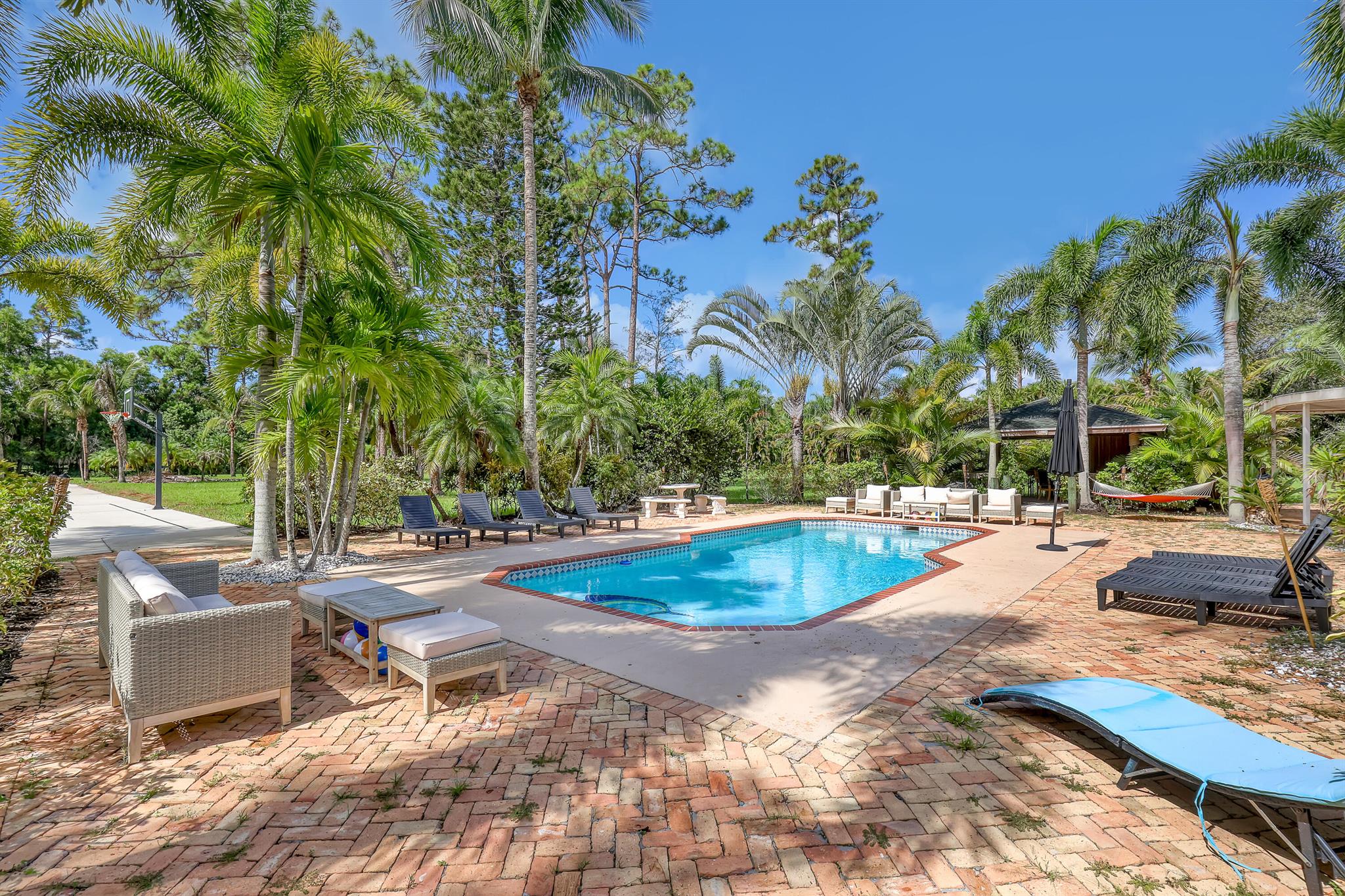 Must see Wellington Estate on over 5 acres, perfect blend of luxury, privacy & resort-style seasonal living. Just minutes from equestrian showgrounds & polo fields. Main house offers 5 bdrms, 3.5 baths, chef-inspired kitchen, brick fireplace & primary suite overlooking heated resort-style pool. Private guest house features 2 bdrms, 1 bath, spacious living area & game room. Outdoor spaces include a large covered patio, tiki hut (w/ electric), Chicago brick pavers, tranquil pond with fountain, gazebo & dock for sunset relaxation, bocce and basketball courts. Fully fenced with electric gate, impact windows, propane generator & 2 covered parking areas--fully equipped for a seamless, luxury seasonal experience. Welcome to Your Home Away from Home!