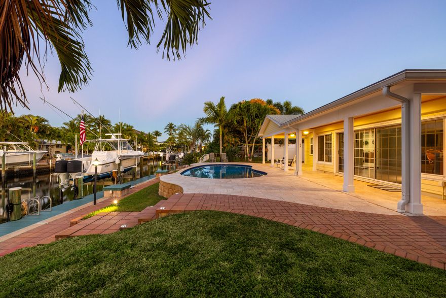 Set along a deep-water canal on a quiet cul-de-sac within one of North Palm Beach's most established, family-friendly streets, this waterfront residence reflects a calm, considered approach to coastal living one that values both refinement and function. With 80 feet of seawall, a decked-over dock, and two boat lifts rated at 16,000 and 12,000 pounds, the property offers seamless access to open water and a lifestyle shaped by time spent outdoors. Inside, light-filled interiors unfold through an open layout that maintains a constant visual connection to the water. The 2024 kitchen is intentionally curated, finished with quartzite countertops, a gas cooktop, wall oven, and new stainless-steel appliances, balancing everyday usability with elegance. The oversized primary suite is set apart as a private retreat, offering dual walk-in closets and a spa-style bath with a two-person Jacuzzi tub, double shower, and dual vanities. Two additional bedrooms with hardwood floors provide flexibility for guests or home office use. A generous family room, anchored by a gas fireplace and a built-in wet bar with beverage refrigerator and quartzite countertops, opens through a full three-panel slider to an oversized, vaulted-ceiling covered patio and expansive paver pool terrace. Outdoors, a custom 2014 pool equipped with an air chiller overlooks the deep-water canal, creating a seamless indoor-outdoor setting well suited for entertaining. Recent updates include a new roof (2024), gas water heater (2025), plantation shutters, crown molding, and solid-core doors, resulting in an enduring expression of modern coastal living.
