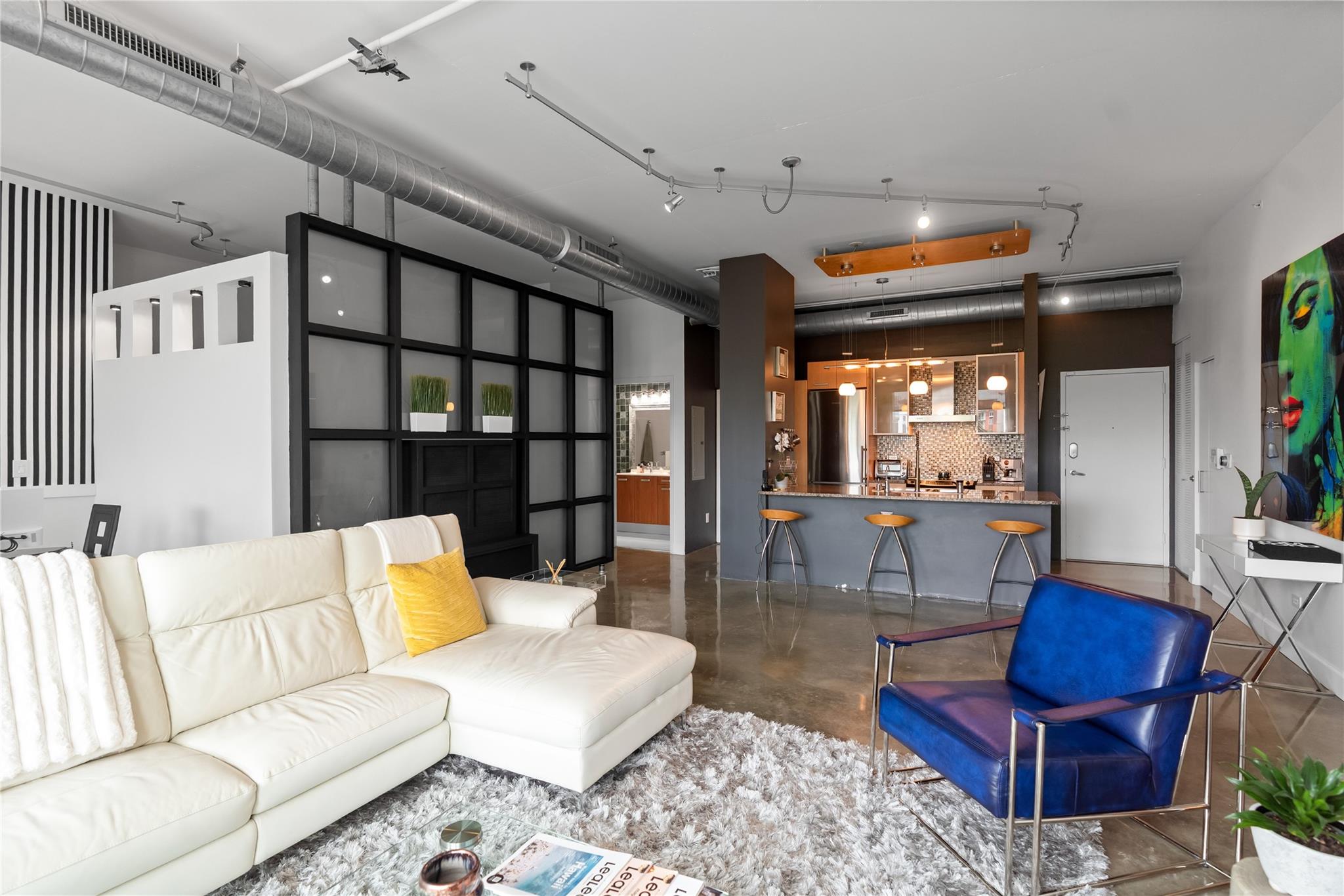 Experience the epitome of urban sophistication in this true industrial-style loft, featuring soaring 11-ft ceilings painted crisp white for a bright, airy feel. Polished concrete floors enhance its authentic city vibe, while 2 bedrooms and 2 full baths offer comfort and style. The gourmet kitchen boasts granite countertops, a glass mosaic backsplash, instant hot and filtered water, plus a brand-new premium refrigerator and LG washer/dryer. A custom room divider with a dual-sided swivel TV separates the living area and guest room, with a recessed TV for sleek appeal. The master retreat showcases a designer accent wall and an opaque glass door for privacy. Modern luxury meets industrial charm in this stunning loft designed for contemporary living.