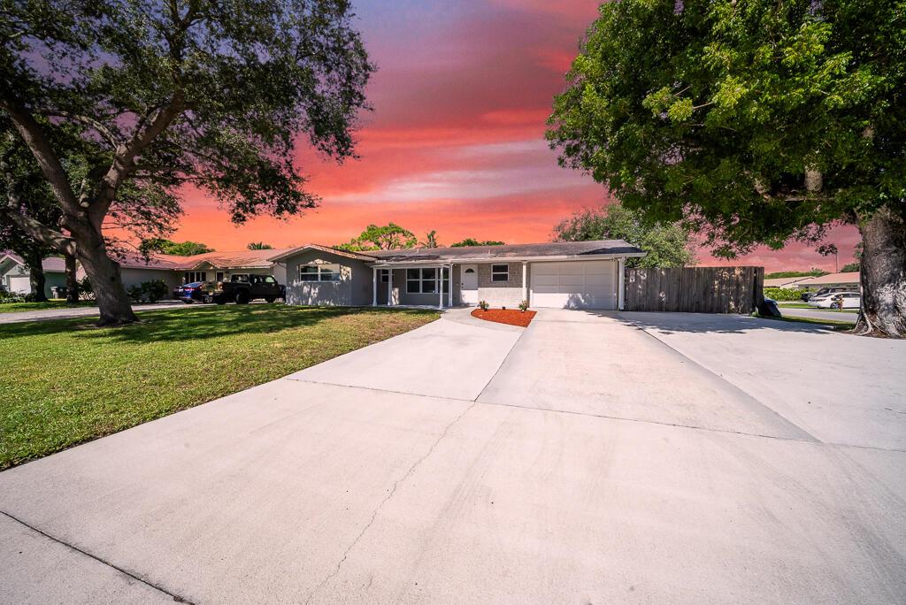 .22 ACRE CORNER LOT IN A NON HOA COMMUNITY! This charming CBS, 2-bedroom, 2-bathroom home is on one of the only streets of unincorporated Jupiter, and offers 1,453 square feet of living space, a 1-car garage and a huge driveway with an extra slab for RV or toys! Step inside to an inviting open concept layout featuring neutral colors, recessed lighting, and smooth ceilings. Enjoy peace of mind with hurricane impact windows and newly relined plumbing (2023). Water heater and AC are 2016. Laminate floors flow throughout and notice a stunning kitchen adorned with stainless steel appliances (2023), a kitchen island with storage, white cabinetry, granite countertops, and classic subway tile.