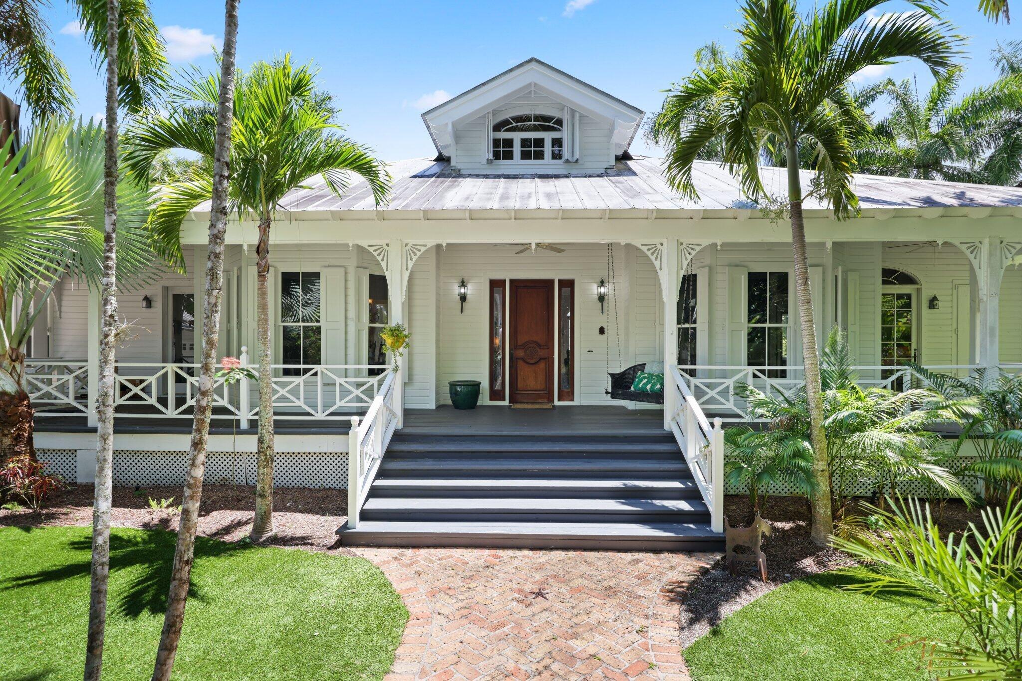 Welcome to your own private oasis in this authentic Key West style home, where every detail captures the essence of tropical living. The entry drive offers an instant sense of being in the Bahamas or on a Costa Rican estate as you're surrounded by a canopy of exotic foliage and specimen plants that create a serene and inviting atmosphere throughout the 2.5 acre property.Step onto the expansive front porch, perfect for leisurely mornings or evening gatherings, and let the gentle sounds of nature welcome you home. Inside, the high wood beam ceilings and rich wood floors lend a warm, inviting feel to every room. The charm of French doors and old-world wood shutters is featured in every room, inviting natural light to each indoor living space.