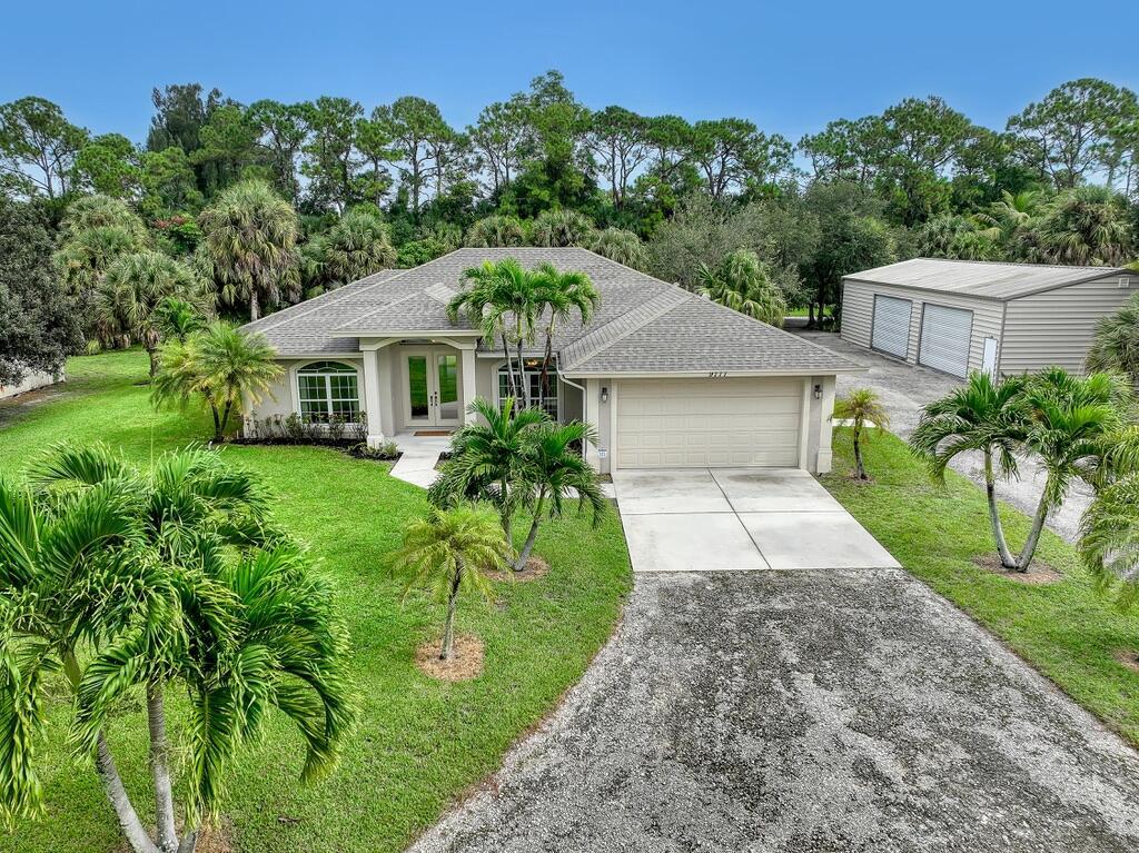 Discover the Jupiter Farms lifestyle in this spacious 4BR/2BA split-floorplan home on 1.33 acres with a 2-car attached garage and an incredible detached 6-car garage/workshop. Step inside to soaring ceilings, an open living area anchored by a fireplace, and a kitchen with granite counters, bar seating, and a sunny breakfast nook. The primary suite includes a spa-like bath with double vanities, a soaking tub, walk-in shower, and built-in makeup vanity. Generous guest bedrooms with large closets provide space and privacy for family or visitors.Enjoy seamless indoor-outdoor living with oversized sliders leading to the screened patio and wide open backyard with room for entertaining, gardening, or pets. A circular driveway and an extended drive to the rear barn offer abundant parking for