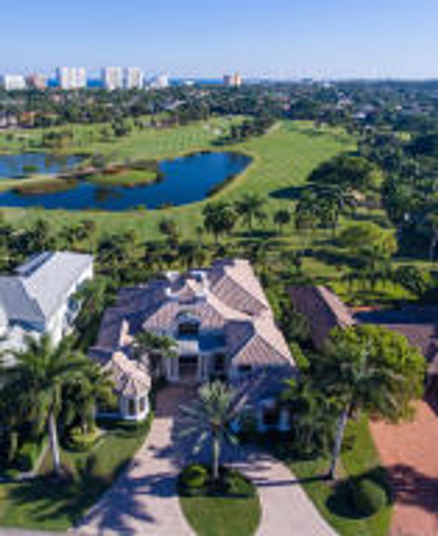 Breathtaking long-range views expand across three lush fairways, centered on a meandering lake, all the way to the beach skyline from this impressive Modern Traditional-style estate facing southeast on the golf course.  Canopied in sumptuous palm trees, the fabulous resort-style outdoor entertainment space provides a dining lanai with grilling station by the sun-splashed pool with waterfall spa.  Manicured tropical foliage also adorns the front grounds where the double-entry drive sweeps to the entrance courtyard.