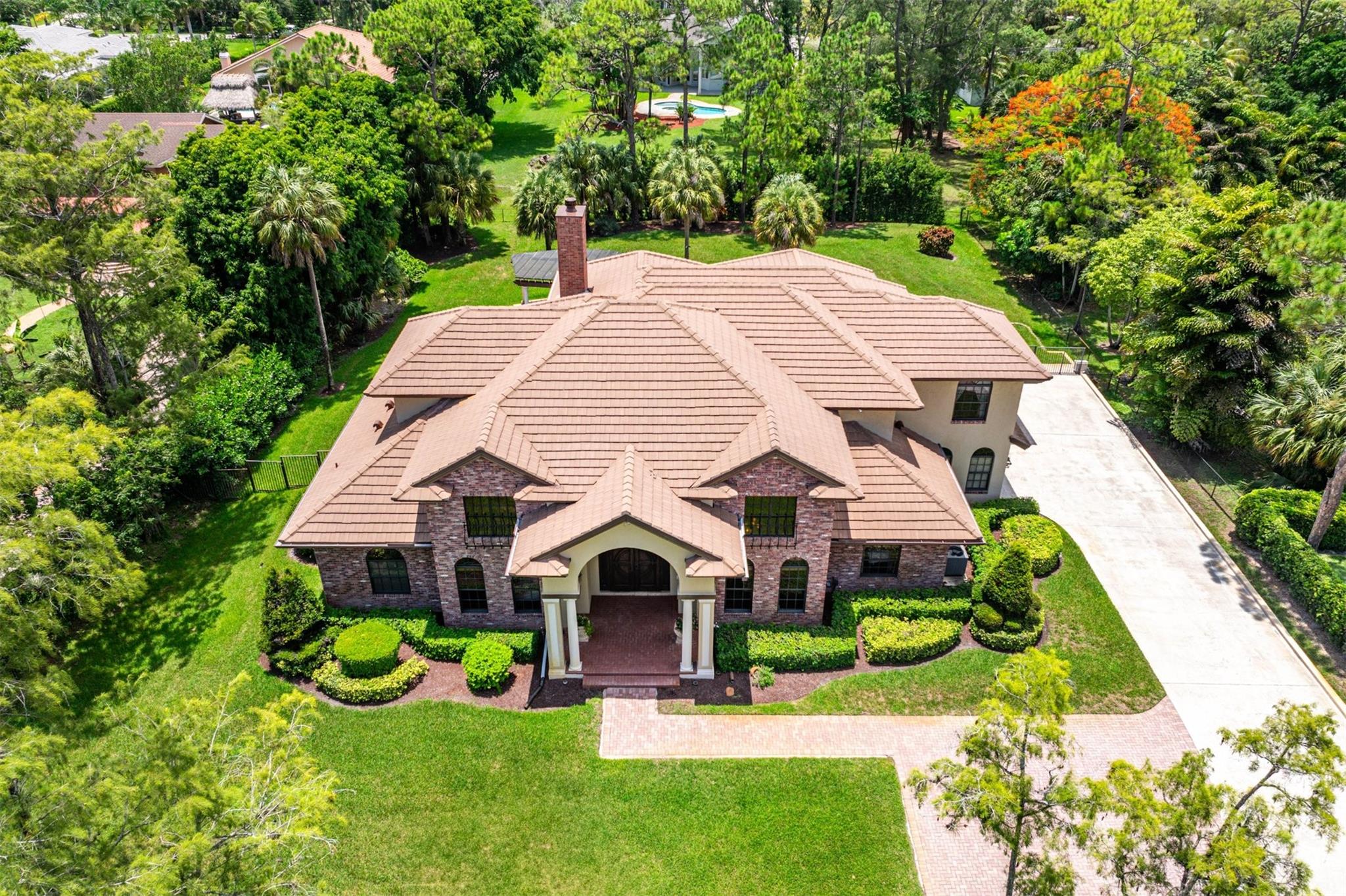 This beautiful estate home is nestled within a 1.09 Acre wooded lot & it will not disappoint. The perfect marriage of timeless Northern grace with the light and airy feel of Florida living. Grand, sun-drenched living areas are framed by impact glass for seamless indoor/outdoor living. A stately exterior offers a long driveway, a manicured expansive front lawn, and a stunning formal entry. The open kitchen/family room impresses with wood cabinetry, top appliances, island, and generous space for gatherings. The first-floor primary suite features a fireplace, spa-like bath, custom closets, and serene pool views. Enjoy a private backyard with a large pool, water features, pergola, summer kitchen, and lush landscaping. Other offerings: 4 Car Garage, Roof 2019, All impact windows/doors, & more!