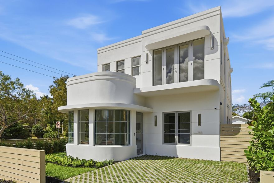 Tucked in the heart of historic Grandview Heights, this striking brand-new Art Deco residence blends architectural character with warm modern living just moments from downtown West Palm Beach in one of the city's most walkable and beloved neighborhoods. Light fills the home through dramatic curved glass windows that create a signature façade and a beautiful front sitting room perfect for morning coffee or an afternoon glass of wine. Inside, large-format porcelain floors, white oak stairs and upstairs flooring, custom cabinetry, and warm brass Kohler fixtures create a refined yet inviting interior. The kitchen features paneled high-end appliances centered around a 36" white Café gas range. Outside a resort-style pool with a tiled LED waterfall & large stone pavers creates a private retreat.