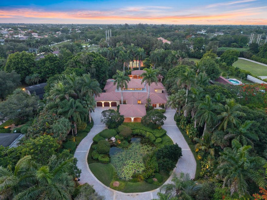 Set on a private 2.34-acre estate in the heart of Sunshine Ranches, this stunning property offers luxury, space, and tranquility. Surrounded by lush landscaping, paved walkways, and a peaceful waterfall pond, it feels like a true Zen retreat. The 5-bedroom home includes an office, maids quarters, and 4.5 bathrooms, featuring marble floors, a bamboo-floor family room, and elegant living and dining areas with a fireplace. Entertain with a custom billiard and bar area or cook in the chefs kitchen with an oversized island and high-end appliances. The grand primary suite offers dual spa baths and his-and-hers closets. Outdoors, enjoy a resort-style pool and spa, two gazebos, a lighted tennis court, and complete privacy surrounded by nature capturing the essence of South Florida luxury living