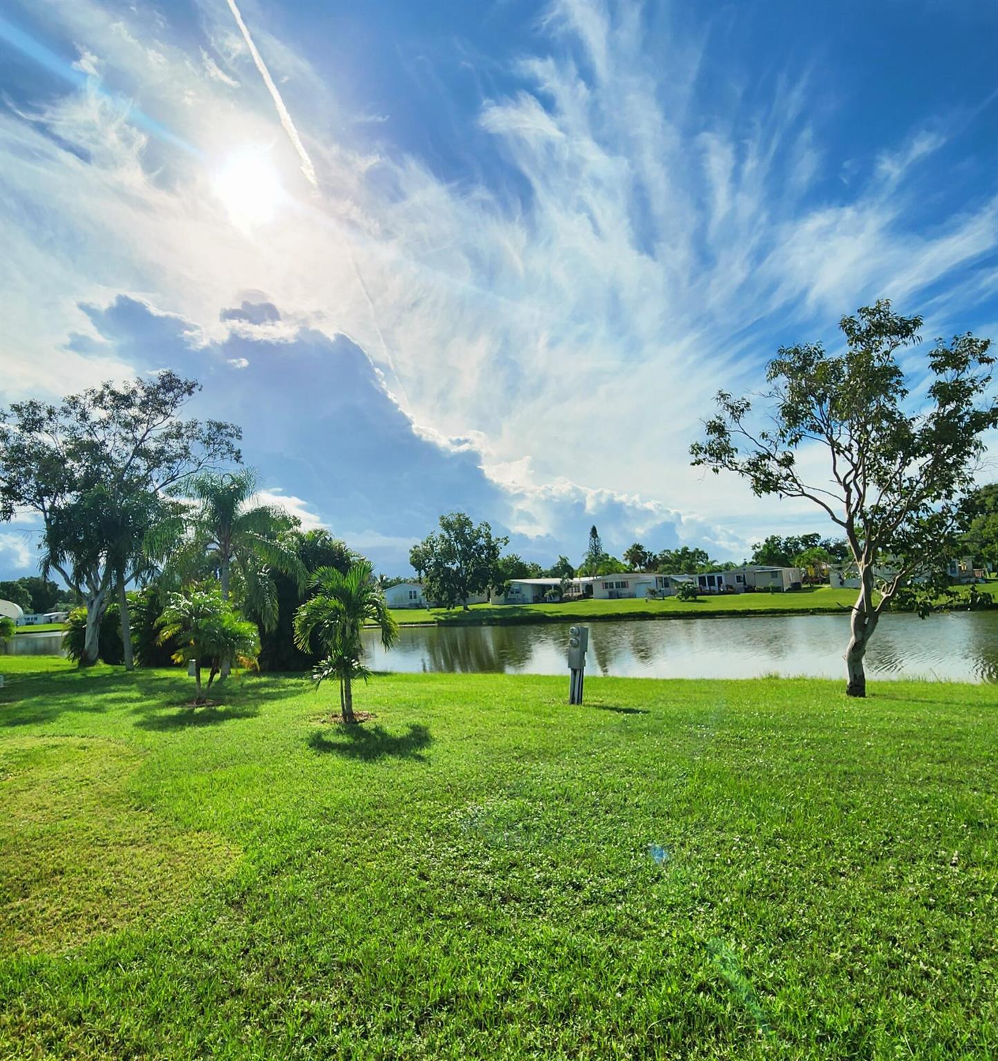 Natural beauty surrounds this 2bed/2bath home, nestled in the back of a CulDeSac on a large corner lot w/ panoramic lake views.Watch ducks & wildlife glide across water & colorful evening sunsets in large window/screened in Florida Rm. Expansive lot offers privacy & space, great for pets, gardening, grilling, entertaining, or soaking in peaceful surroundings. Recent updates include a 2020 roof, 2023 AC & 2022 carpet/flooring, WaterHtr 2020. PRIME LOCATION; near beach, grocery stores, post office, banks, hospitals, pharmacy & more! Lot rent of 1080.98 includes private golf course (no fees to play) heated pool, fitness, pickleball, tennis, shuffleboard, bocce, gym, library, card games, MahJong, Bible study, wood workshop, parades, dinners, dances, trips & more! Lawn cutting & trash included