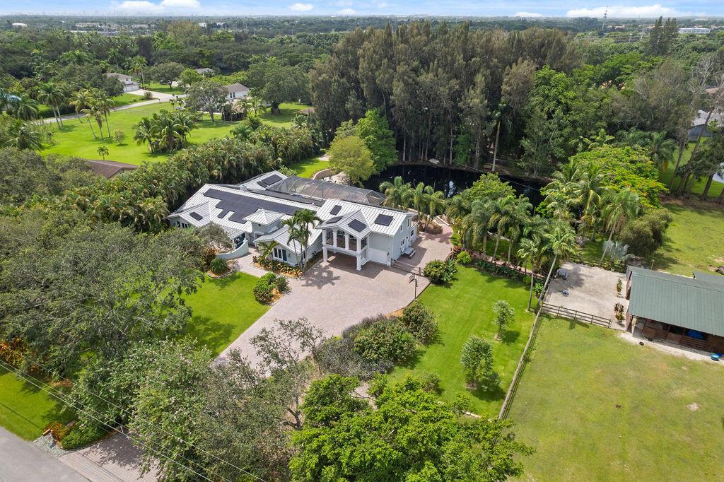 If you are looking for Shangri-La, look no further! Situated on 2.5 Acres of a Tropical Oasis, this home and property truly have it all! The 1/2 Acre filtered pond with fountain is surrounded by beautiful enormous pine trees offering a park like setting with lighted paver walk ways and gorgeous sitting area.There is also a 3 stall barn for horses with feed and adjacent air conditioned tack room/office as well as chicken/hen coops and room for ring and paddock! Features include, Metal Roof, Solar Panels, Newly resurfaced Resort Style Saltwater Pool with new heater, slide and Hot Tub! Outdoor Kitchen, gas fireplace, Complete Impact Glass Windows, Gourmet kitchen with large island, Newer Bosch Induction stove top, Newer Refrigerators, New Bosch dishwasher,