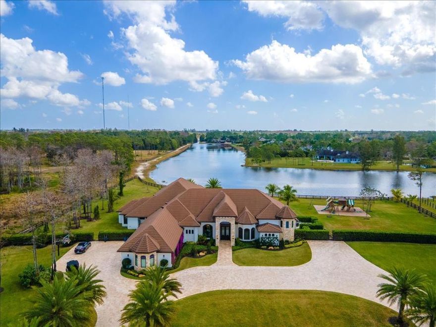 For the most discriminating taste, this exquisite estate features a 6 bedroom, 6-1/2 bath home that was built in 2017 with no expense spared!  From the moment you drive through the gates of this property, you will find that it is meticulously maintained with lush landscaping.  The 20' arched entryway boasts beautiful stone columns and 8' custom mahogany wood double doors with impact glass.  In addition to the 6 bedrooms, there are also a spacious game room with full bar and full bathroom, a craft room with two works spaces and sink, an office, a wine closet, and butler pantry.  The state-of -the-art kitchen features quartz countertops, stainless steel appliances, including a Sub-Zero refrigerator, Thermador 6 burner gas stove and so much more! The home has impact windows and French doors, a whole house Generac 80kw generator with 1,000 gallon propane tank, reverse osmosis Aqua Soft System and electric remote control operated blinds throughout. 
There is a covered patio area with a double-sided gas fireplace and electric roll down screens overlooking the tranquil lake. The outdoor kitchen features quartz countertops, stainless steel appliances including a Bull refrigerator, 4 burner alfresco grill, smoker, fryer, sink and ice maker.  The heated saltwater pool/spa is extremely relaxing with seating benches. The vacant lot across the street is also available (see RX-10336053) for additional acreage to build your dream farm! Don't miss out on this gated 5-acre property in the sought-after equestrian Homeland community!!