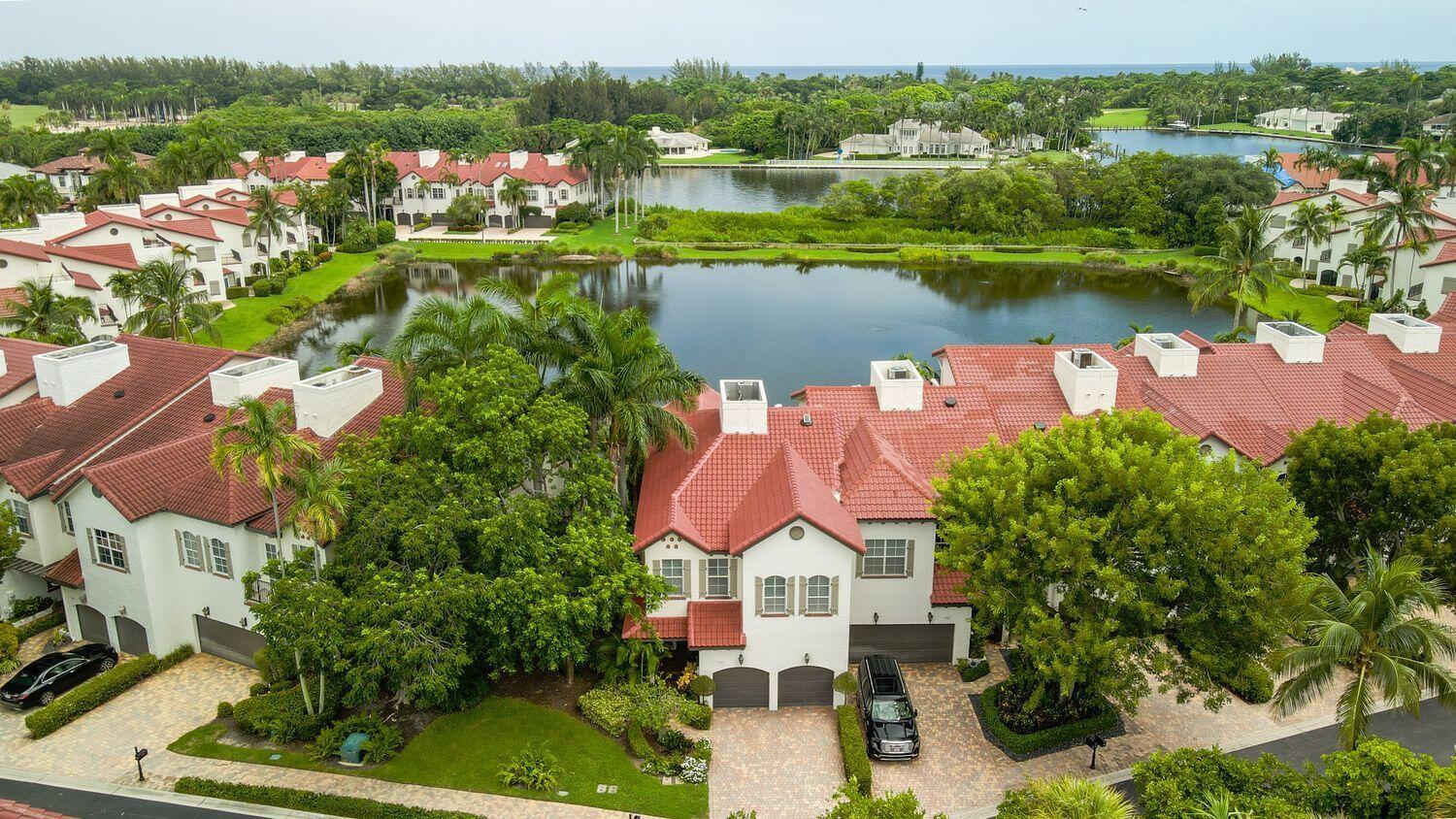 This upgraded Magellan model townhome offers 2,900 sqft with lake and Intracoastal views. It features professionally landscaped exteriors, paved driveways, and a motorized screened-in porch. Inside, find wood flooring, 10-ft ceilings, and an open floor plan centered around a chef's kitchen with quartzite countertops, stone accent wall, induction range, and recent appliances. A custom bar with wine fridge enhances entertaining. The home includes three bedrooms, an upstairs laundry room, and a large closet for elevator installation. The primary suite offers his-and-hers bathrooms, a private balcony, and a secondary patio. Additional features include two A/C units, a new marble bathroom, impact windows, newer roof, and full home security.