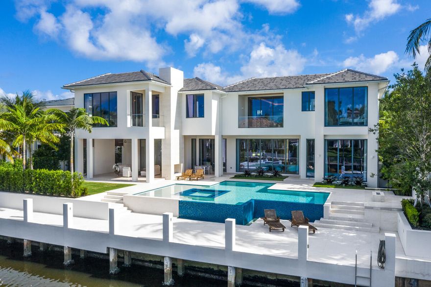 Crafted by Sarkela Corporation, 249 Alexander Palm Road is a striking waterfront estate positioned along one of Royal Palm Yacht & Country Club's most coveted streets, offering direct Intracoastal and ocean access. A gated approach reveals a commanding arrival, where marble-clad architectural elements set the tone for the level of detail carried throughout. Inside, the residence unfolds with a refined European aesthetic, defined by exceptional materials and a cohesive, contemporary design vision. Custom lighting by Terzani, curated marble selections, bespoke wall treatments, and premium European oak flooring establish a sense of continuity and quiet distinction across the interiors.  Spanning 8,815 square feet, the layout is both expansive and fluid, designed to accommodate both formal entertaining and relaxed daily living. A dramatic two-story living room is anchored by a 24-foot marble fireplace, complemented by a formal dining room with a glass-enclosed wine display, a media lounge with bar, a private office, and a well-appointed kitchen featuring cabinetry by Duccini Milano. The primary suite occupies a private position on the upper level, offering a generous sitting area facing the water, along with dual baths and dressing rooms designed for comfort and privacy. Outdoor spaces are also considered, with manicured grounds framing a covered summer lounge, an outdoor kitchen, a linear fireplace, and an infinity-edge pool with an integrated spa and a sun shelf. Furnishings curated by designer Raquel Mothe enhance the home's architectural clarity and material palette. A private deep-water dock, finished with marble decking and equipped with power and water, accommodates large vessels and provides immediate access to open water. This residence is designed for those who value precision, scale, and a seamless waterfront lifestyle.