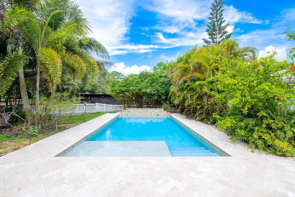Experience the best of both worlds with this beautifully maintained pool home in Jupiter Farms--offering peaceful country living just minutes from all the conveniences of town. This versatile 4-bedroom, 3-bath layout is ideal for multi-generational living or potential rental income. The attached efficiency apartment features a private entrance, full kitchen with stainless steel appliances, vinyl flooring, quartz countertops and its own HVAC system. The main residence is a 3-bedroom, 2-bath split floor plan with a 2-car garage, high vaulted ceilings, LED lighting, and great natural light. The open kitchen overlooks the beautiful pool and travertine patio, perfect for entertaining. The primary suite includes a private office, walk-in closet, soaking tub, separate shower, and dual vanities.