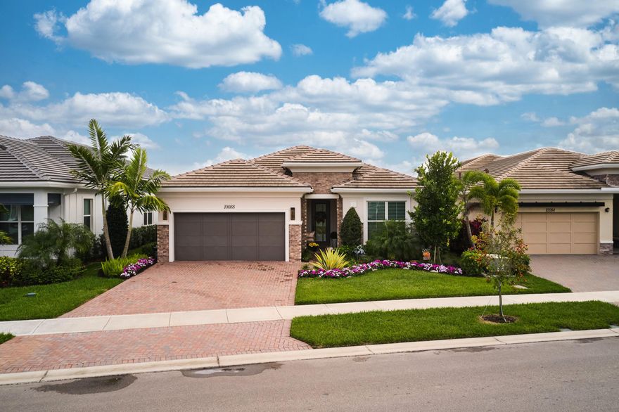 Welcome to this beautifully appointed 2023 single-story residence in the gated Regency neighborhood of Avenir. Offering 3 bedrooms, 2.5 bathrooms, a versatile flex space currently utilized as a den, a 2-car garage, and 2,434 square feet of thoughtfully designed living space on a 6,891-square-foot lot, this home blends modern comfort with refined style. Wood-look white-oak-tone tile and a soft linen-hued palette create a warm, cohesive aesthetic throughout the entire home. The main living area showcases an open-concept design that seamlessly connects the living room, kitchen, and dining room. The spacious living room is enhanced by a tray ceiling with recessed lighting and a striking chandelier, while sliding glass doors invite abundant natural light. The adjacent chef's kitchen features wood-shaker cabinetry in complementary off-white and taupe tones, a stainless-steel appliance suite with gas range, marble-look quartz countertops, and an expansive island with apron sink, storage, and seating. The dining room, framed by large windows and patio access, is anchored by a modern light fixture that adds character to the space. The primary suite offers a peaceful retreat with its tray ceiling, dramatic chandelier, and generous dimensions that easily accommodate a seating area. The spa-inspired en-suite bathroom includes dual vanities with quartz countertops, gold fixtures, a dedicated dressing and makeup station, a glass-enclosed shower, and a soaking tub overlooking the garden. Two additional bedrooms provide comfortable accommodations for family or guests, while the flexible bonus room, currently configured as a den, offers adaptability for a home office, media space, or hobby room. Each secondary space benefits from excellent natural light, with one bedroom appointed in soft Berber carpeting. A well-designed laundry room with built-in cabinetry, sink, and high-efficiency appliances adds everyday convenience. Outdoor living takes center stage with an expansive covered patio featuring a full summer kitchen and dining area. Beyond, an open patio provides additional seating around a sparkling pool with built-in sun shelf, set opposite a decorative waterfall wall. Lush tropical landscaping and a full privacy hedge complete this serene backyard retreat. This inviting and sophisticated home offers the best of modern living in one of Avenir's most desirable neighborhoods, an ideal setting to relax, entertain, and fully embrace the South Florida lifestyle.