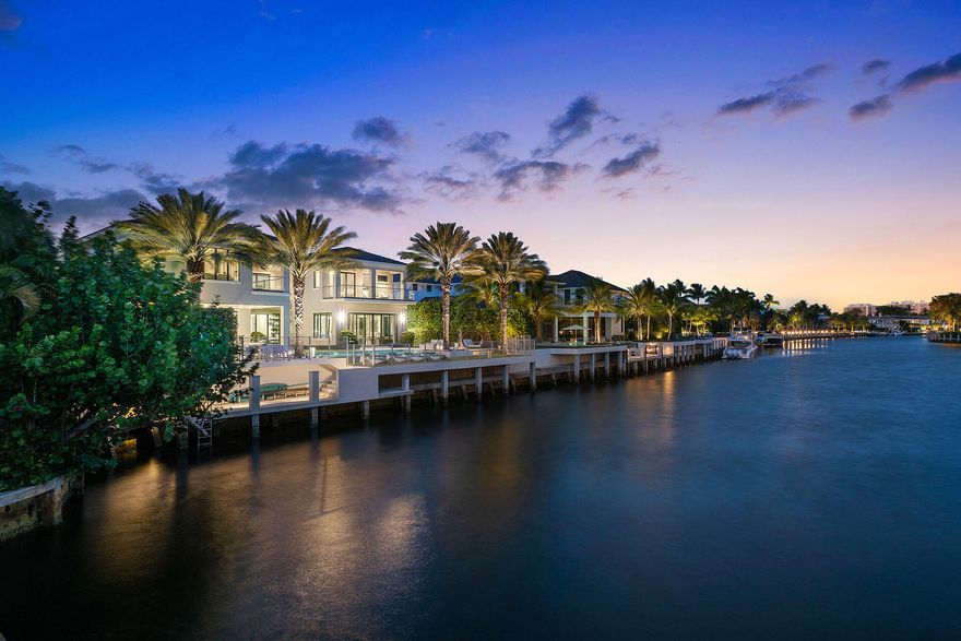 A commanding presence on Royal Palm Yacht & Country Club's Grand Canal, 290 South Maya Palm Drive is a masterpiece of modern coastal luxury by Bloomfield Construction. This waterfront estate spans over 9,000 square feet, offering five impeccably designed bedrooms and 6.2 baths, all crafted for those who demand the finest design and craftsmanship. A soaring two-story gallery foyer sets the tone for the home's exquisite interiors, where striking agate accents, floor-to-ceiling marble, and recessed architectural lighting create an ambiance of understated grandeur. The estate's expansive club room, featuring a luminous resin bar, is designed for lavish entertaining, while motorized sliding glass doors seamlessly connect indoor and outdoor living.