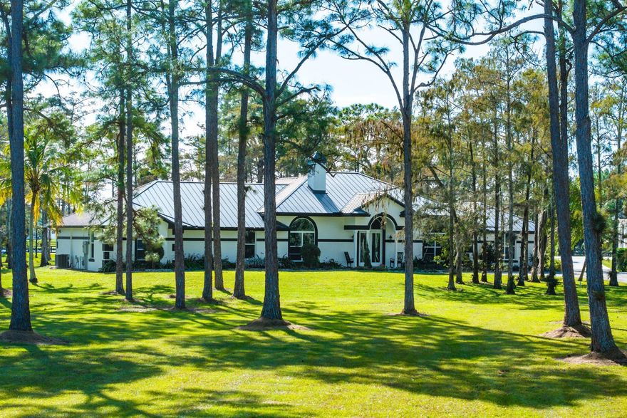 Experience privacy on 5 acres in the Homeland equestrian community. This home sits behind a gated, tree-lined driveway with lush landscaping and a newly upgraded front gate. Upgrades include a 2018 metal roof, impact doors and windows, a concrete safe room, poured driveway, travertine walkways, and all bathrooms redone with marble countertops. The master suite and closet were redesigned, plus a connected mother-in-law suite. Wood-look tile, volume ceilings, crown molding, and a renovated kitchen with granite and stainless appliances. Outdoor kitchen, resurfaced pool, hard-wired cameras, RO water, blinds, fixtures. Par-3 golf hole with stadium lighting and misting fans, commercial playground enhance your private outdoor amenities. Separate two-story garage for all your toys.