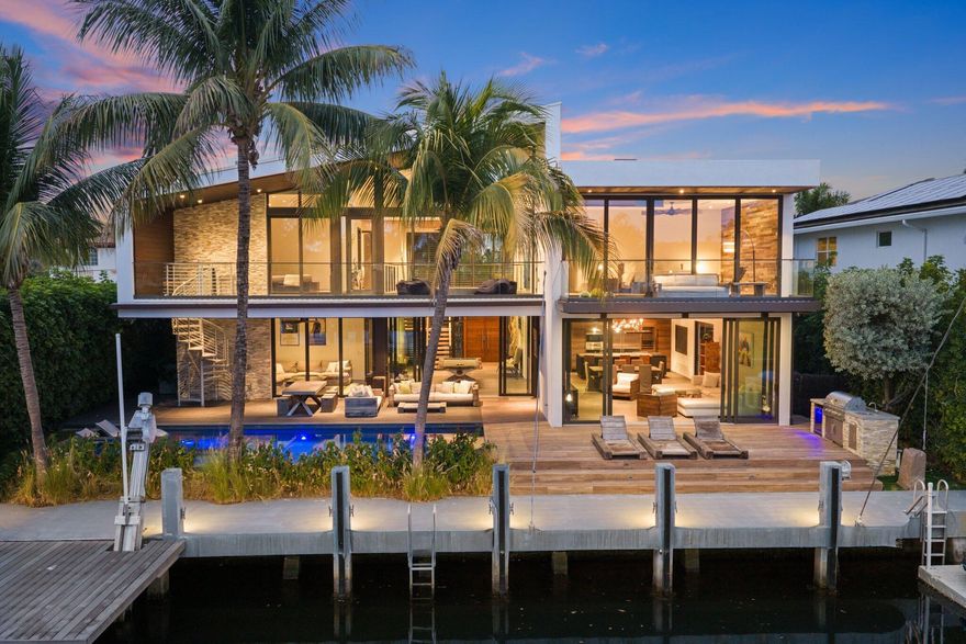 Stunning contemporary 5-bedroom + office waterfront residence offering true boating freedom with no fixed bridges to the Intracoastal Waterway. Upon entry, a dramatic great room with soaring vaulted ceilings and floor-to-ceiling glass creates an immediate sense of scale and light, framing views of the tropically landscaped pool, patio, and canal beyond. The open-concept layout seamlessly connects the kitchen, dining, and family/media areas, ideal for both everyday living and entertaining. Chef's kitchen with a large center island with seating for five, Wolf & Sub-Zero appliances, built-in wine storage, beverage drawers, & ice maker. The first-floor ensuite bedroom is currently configured as a media room overlooking the pool and canal, complete with automatic drop-down shades and projector system. A powder room with floating wood vanity completes the main level.Upstairs, the primary suite is a private retreat with dual covered balconies, automatic drapes, spa-style bath with soaking tub, rain and wall shower, water closet, and a custom walk-in closet with island cabinetry. Three additional ensuite bedrooms are located on the second level, two with balcony access; one is currently used as an office. A maid's quarters with full bath adds flexibility.Outdoor living is elevated with a heated pool, summer kitchen, and spiral staircase connecting the upper balcony, featuring a gas fire pit to the pool deck below. Boaters will appreciate 80 feet of waterfront, a 40-foot boat mooring area, dual Wave Runner lift, and a 25,000-lb boat lift. Additional features include Crestron lighting, built-in speakers throughout, Nest climate control and video surveillance, full impact windows, full-house propane generator, 1,000-gallon propane tank, Aqualink pool system with app control, stone tile flooring, and a utility room with Electrolux washer/dryer and storage.

A rare opportunity to own a modern waterfront home designed for effortless indoor-outdoor living and serious boating.