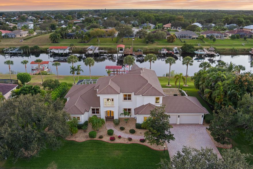 Welcome to your own private paradise in the heart of Port St. Lucie. This stunning custom Mediterranean-style CBS estate offers the ultimate in luxury waterfront living with over 150 feet of frontage along the C-24 Canal. Designed for boating enthusiasts & entertainers alike, the property features a private dock with boat lift, a tiki hut perfect for sunset gatherings, & quick access to the nearby public boat ramp. This five-bedroom, five-bath residence offers an exceptional floor plan with a first-floor guest suite, home office, family room, dry bar, balcony, residential elevator, & a three-car garage, all thoughtfully designed for comfort, functionality, & elevated Florida living. A screened pool & spa create a true resort-style outdoor retreat, complemented by a summer kitchen with grilling station, cabana bath, fire-pit area, & lush tropical landscaping. Inside, soaring ceilings & travertine floors set the tone for refined living. The chef's kitchen features dual sinks, dishwashers, ovens, refrigerators, an eight-burner gas cooktop, granite countertops, wine coolers, icemaker, & generous prep space. The primary suite offers dual walk-in closets, a sitting area, & a spa-inspired bath. Additional highlights include impact windows & doors, Taylor foam wall insulation, Icynene ceiling insulation, surround sound, & central vacuum. Located in the gated enclave of South River Shores with low HOA fees, minutes to the Turnpike, shopping, dining, & Tradition.