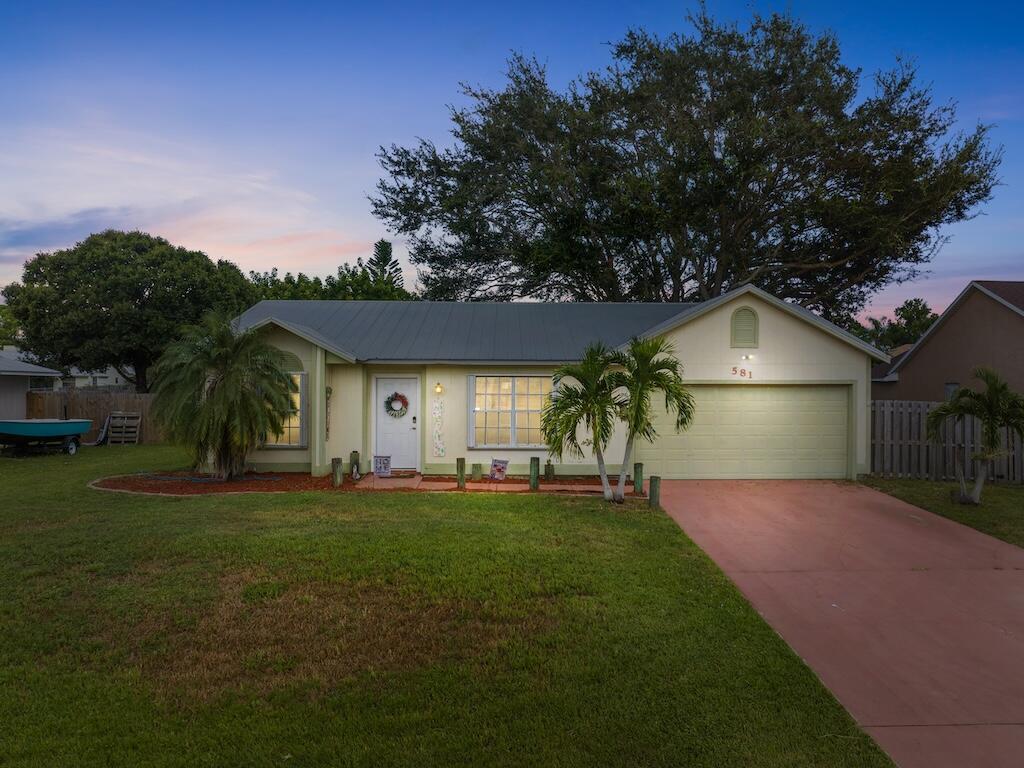 Step into this inviting 3 bedroom, 2 bath home in central Port St. Lucie. Perfectly suited for first time buyers or anyone seeking a cozy home in a great location. Built in 1990, the interior features vaulted ceilings in the living, dining and kitchen areas, laminate ''wood'' flooring throughout the main rooms and durable ceramic tile in the kitchen. The private maine suite sits opposite two guest bedrooms and offers a walk-in closet and an ensuite bath. Accordion shutters protect all but one window, while a 2022 metal roof gives you long-term peace of mind. Outside, enjoy a screened-in patio overlooking a generously sized yard. A two-car garage provides extra storage or workshop space. Conveniently located just 13 minutes to Tradition Village Center, 15 minutes to St. Lucie West shopping,