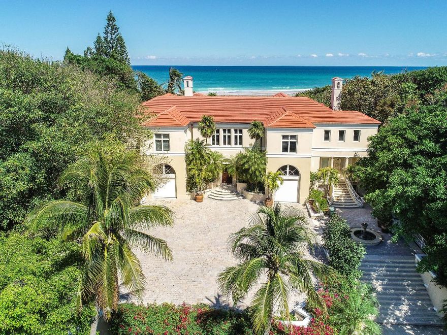 A singular opportunity in the secluded enclave of Jupiter Island, this unique property spans 142' of direct ocean frontage. Unfurling back from the waterline a sprawling waterfront estate rests on over 2 acres. A private drive situated under a lush canopy of banyan trees ushers guests to the stately entrance of the home. To the southwest, nestled below the classically inspired courtyard, the secluded pool area complete with pool house is its own oasis. Inside, a tasteful foyer opens to the soaring ceilings of the main living room, a welcoming prelude to the home's four bedrooms and six and a half baths. Floor to ceiling windows and French doors lend to the airy aesthetic of the space providing sweeping vistas of the Atlantic waters beyond...tucked into the northeast corner of the room: a full wet bar. A sunny breakfast nook and a warm, open kitchen with best in class appliances betwixt bespoke cabinets continue the inviting common spaces. An elegant sitting room with an expansive travertine fireplace and private office with Mahogany built ins and accents round out the ground floor. The second-floor master suite with unencumbered Ocean views boasts a private balcony overlooking a private beach access...superbly executed waterfront living.