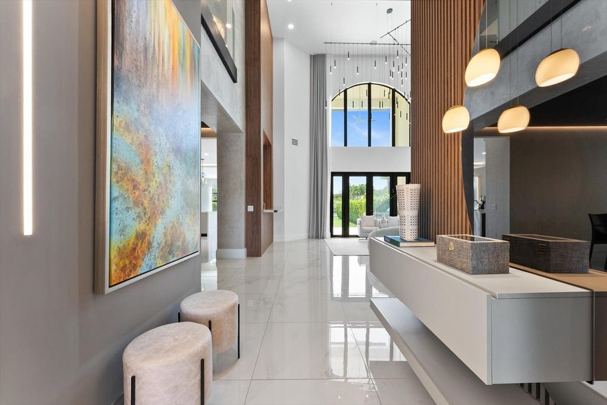 Reimagined in 2023, this 4-bedroom plus office/loft residence (optional 5th) is a modern Mediterranean showpiece in The Bridges, blending sophisticated design with everyday functionality. A circular driveway and professionally designed landscaping create exceptional curb appeal. Inside, 32x32 glossy porcelain floors on the main level and bamboo flooring upstairs are complemented by Control4 automation and a Sonos sound system for seamless living.  The entry is defined by a custom wood slat feature wall with integrated LED lighting and designer pendants, setting a refined tone. The sitting room showcases double-volume ceilings and a floor-to-ceiling feature wall with a sleek linear fireplace, while walls of glass bring in natural light and frame views of the summer kitchen, pool, and waterfront beyond. A separate dining room features a stretched vinyl ceiling, cove lighting, and a statement chandelier, creating a striking setting for formal dining. Adjacent to the kitchen, a custom built-in wet bar features illuminated shelving, a stone countertop with prep sink, and a wine refrigerator, creating an elegant space for entertaining. The chef's kitchen is appointed with dramatic Panda marble countertops, a waterfall island, custom cabinetry, and Wolf and Sub-Zero appliances, along with a breakfast bar, designer lighting, and a sunlit dining area. The adjoining family room is anchored by custom built-ins and walls of glass that frame sweeping views of the pool, waterfront, and The Bridges' signature waterfall feature, creating seamless indoor-outdoor flow. Outside, a heated saltwater pool with spa, sun shelf loungers, motorized cabana, and fully equipped summer kitchen is surrounded by lush, professionally designed landscaping and long water views, offering a true private retreat. Beyond the main living spaces, the primary suite serves as a private sanctuary with a coffered ceiling, custom wall detailing, and expansive windows showcasing serene waterfront views. A bespoke passage with custom built-ins and a fully outfitted dressing room leads to the spa-inspired bath, wrapped in large-format stone and featuring dual vanities, sculptural lighting, a heated towel warmer, and a Kohler steam shower with multiple showerheads, digital controls, and integrated audio. An electronic bidet and a rare private dry bar with refrigeration and coffee service complete this exceptional retreat. Additional features include two newer A/C units with RGF Reme Halo whole-home air purification, activated charcoal whole-house water filtration with in-garage shutoff, a Tesla charger, a new 2026 tankless water heater, and a 10-camera security system—further enhancing the home's comfort, efficiency, and peace of mind. Located within The Bridges in Delray Beach, residents enjoy access to a 17,000-square-foot clubhouse, resort-style pool and spa, fitness center, tennis, pickleball, indoor and outdoor basketball, and a vibrant array of social and lifestyle amenities, completing the offering of one of South Florida's premier gated communities.