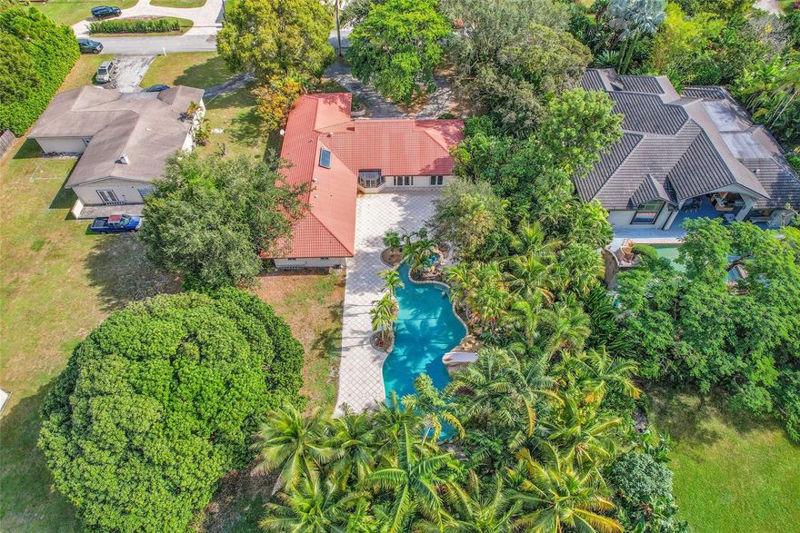 Welcome to a stunning residence nestled within historic Plantation, showcasing timeless elegance. This four-bedroom home features a well-designed split floor plan, offering both privacy and space. Set on over an acre of landscaped grounds, the property includes a serene tropical pool for relaxation and entertaining. A grand circular driveway leads to an inviting entrance, while the spacious kitchen—equipped with a high-end KitchenAid refrigerator—serves as the heart of the home. The layout includes a luxurious primary suite with a large walk-in closet and impact windows for security and energy efficiency. With expansive outdoor spaces and a seamless blend of indoor and outdoor living, this home offers the perfect retreat for refined living.