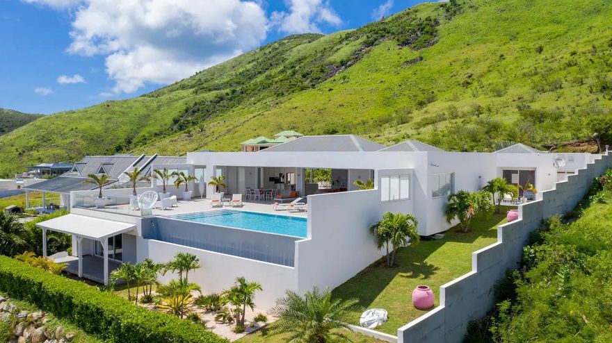 Channeling understated luxury and panoramic Caribbean beauty, this 350 m² contemporary villa is perched above the sea with sweeping views of St. Barth. Privately located at the end of a quiet cul-de-sac with secured access, the home is designed to frame the horizon from every room in a luminous, serene setting. The main residence features a triple split floor plan with 3 spacious en-suite bedrooms, while a separate apartment with private 70 m² sea-view terrace adds a 4th bedroom. The custom kitchen is fully equipped with high-end appliances including double ovens, and a wine cellar. Outdoors a 240 m² terrace surrounds the infinity pool, embraced by a lush tropical garden. This home offers both refined living and strong investment potential in one of the Caribbean’s most desirable enclaves.