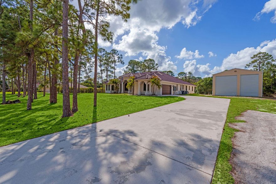 Welcome to this home in The Acreage, offering 4 bedrooms plus a den, 3 full bathrooms, and a half bath, all set on an expansive 1.14-acre lot with a 2-car attached garage and an impressive 1,800 sq ft detached steel shop. The home has been freshly painted and features hurricane impact windows and doors, a tankless hot water heater, reverse osmosis system, generator hookup, and newer water system. Enter through the double front doors into a bright and spacious interior with 12' ceilings, a welcoming foyer, vertically laid porcelain flooring, and abundant natural light throughout. The kitchen is designed for both everyday living and entertaining, featuring a large island with storage, granite countertops, stainless steel appliances, glass display cabinetry, a generous walk-in pantry, and a  breakfast nook overlooking the surrounding property. The split floor plan provides privacy and comfort with real wood floors, detailed millwork, tray ceilings, French doors, and spacious living areas. The primary suite offers peaceful views and includes dual walk-in closets, granite vanities, a large walk-in shower, and a relaxing jacuzzi tub.  Step outside to enjoy the 34' x 16' covered lanai, surrounded by mature pine trees and tropical palms that create a quiet and relaxing outdoor setting. The property also features a substantial 60' x 30' Eversafe steel building with a 21' ceiling, large roll-up doors, 200-amp service, and multiple 220 and 110 outlets, providing exceptional flexibility for storage, hobbies, or workspace.  Located in the desirable Acreage area of Palm Beach County, this home offers peaceful country-style living while remaining just minutes from shopping, dining, parks, and equestrian facilities. Convenient access to Florida's Turnpike, I-95, Palm Beach International Airport, and the area's beautiful beaches makes commuting and travel simple while still enjoying the privacy and space this unique property provides. Make this luxurious retreat your own and experience refined living in this exceptional residence.