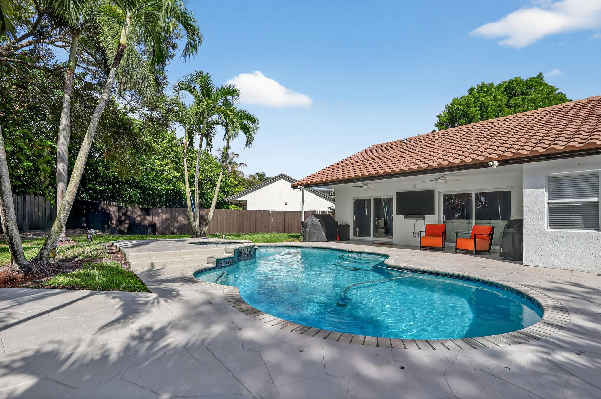 This meticulously maintained property features a spacious 15,263 sq ft lot with a fully fenced backyard, complete with established fruit and palm trees. The open floor plan boasts vaulted ceilings and freshly painted interiors with recessed lighting. Enjoy a spacious covered patio, perfect for entertaining by the pool and jacuzzi. The den, currently a fourth bedroom, can also serve as an office. The kitchen is equipped with a steel-less appliances, white cabinetry, granite countertops, and a stunning waterfall countertop. Both bathrooms feature contemporary designs and high-end finishes. The master suite includes impact windows and doors, and a walk-in closet. Additional highlights include new doors, baseboards, flooring, a newer AC and roof installed in 2016 and security cameras.
