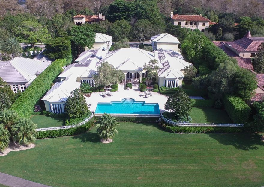 This sprawling property is marked by an elegant style with a subtle tropical feel, and is one of the finest estates Palm Beach Polo Golf and Country Club has to offer. Rarely does an exquisite home of this magnitude become available in the elite gated Bridle Path neighborhood, near the area's world famous equestrian festivities. Upon entering the gates to the property, the stately motor court features two spacious garages built to accommodate four vehicles. Expertly designed by Laszlo Wagner of the Landfall Group for the current owner, the main house provides over 9,000 feet of air-conditioned living space. The home boasts a pleasant mix of limestone and wormy chestnut floors, neutral decor, formal living and dining rooms, 2 fireplaces, and a remarkable cherry paneled library.