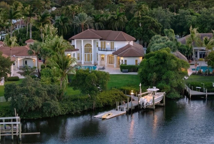 Transitional riverfront estate with attached guest house on an oversized .7 acre private waterfront lot within an exclusive gated community. This functional residence features 6 bedrooms, 5.1 baths, 2 living areas, formal dining room, guest quarters, and three-car garage, with an open-concept floor plan, soaring ceilings, crown molding, and luxury vinyl flooring throughout. Recent improvements include a 2019 roof, impact glass windows and doors, and newer air-conditioning systems. The 2021 reimagined chef's kitchen showcases new kitchen cabinets with recessed lighting, quartz countertops with Galley sink and double faucets, a Sub-Zero refrigerator, and a Wolf gas range, flowing seamlessly into the expansive living and dining spaces.  ( See supplement remarks) Large covered outdoor entertaining areas overlook the resort-style saltwater pool and spa, all set against the stunning backdrop of the wide Loxahatchee River.  A true boater's paradise, the property includes a private deep-water dock with a large boat lift located on the main fork of the river, offering direct access to exceptional waterfront cruising. Surrounded by a large private backyard and lush tropical setting, this rare offering combines luxury, privacy, and premier riverfront living.