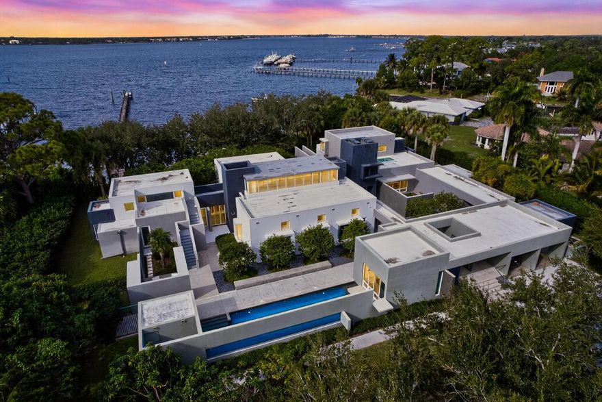 Spanning more than 200 feet of protected shoreline, this rare double riverfront estate offers an exceptional balance of privacy, scale, and uninterrupted St. Lucie River views.  With unobstructed water vistas stretching endlessly across the horizon, the residence offers a daily spectacle of panoramic sunsets—an ever-changing canvas of color, light, and reflection.
Spanning approximately 7,500 square feet, the home is a masterful expression of modern architecture thoughtfully integrated into its natural surroundings. Expansive walls of glass dissolve the boundary between indoors and out, framing the river from nearly every room and allowing light, sky, and water to become defining elements of the living experience. The result is a residence that feels both architecturally bold and deeply serene.   Designed for refined yet effortless living, the home features five spacious bedroom suites and five-and-a-half baths, complemented by two private offices, each positioned to capture tranquil views of the pool or river. A dedicated guest suite offers an added layer of privacy and comfort, creating a welcoming retreat for extended family or visiting guests.
For boating enthusiasts, a 360-foot private dock extends gracefully into the river, offering immediate access to the St. Lucie Inlet and the Atlantic Ocean beyondplacing world-class yachting, fishing, and cruising just moments from your doorstep.
The outdoor living environment is nothing short of extraordinary. Lush, exotic landscaping, centuries-old oak trees, and a series of thoughtfully designed water features create a setting of rare tranquility. A koi-filled courtyard pond and layered backyard pond enhance the sense of calm, while multiple intimate courtyards invite quiet reflection or elegant entertaining. Every element has been curated to foster a seamless connection to nature while maintaining an unmistakable sense of sophistication.
This is more than a riverfront residenceit is a private sanctuary, where modern design, natural beauty, and understated luxury converge in one of South Florida's most compelling waterfront settings.