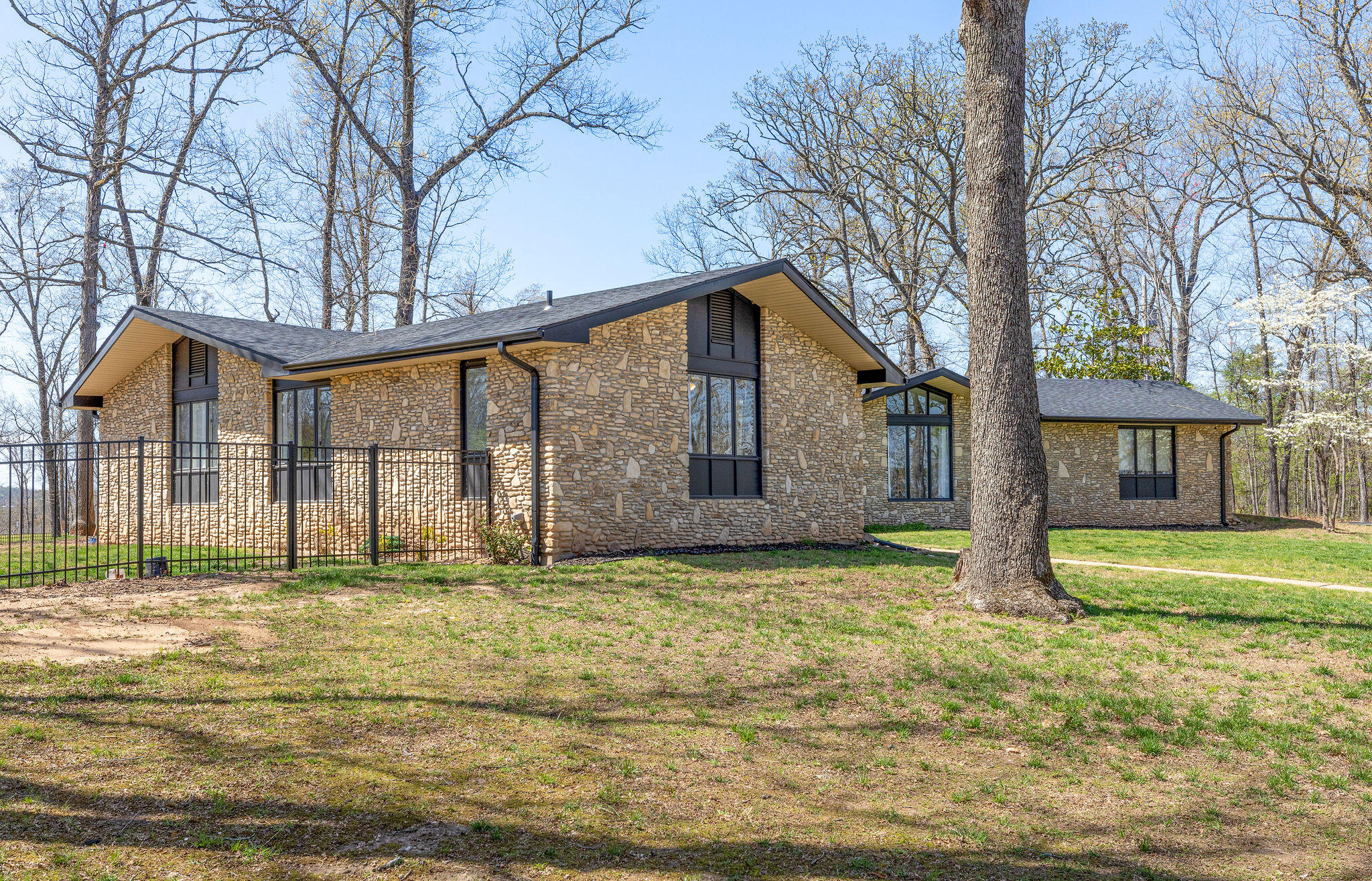 Five minutes from Branson's Target & Super Walmart, drive down a paved, tree-lined, private lane onto five beautiful acres to this 4,600 sq.ft stone home with a heated/cooled shop/warehouse.The immaculately renovated home features 3 bedrooms on the main floor, and 2 non-conforming bedrooms on the stormproof basement level. Main level bedrooms include a spacious master bedroom with patio door to outside sitting area, as well as a deep and extra-long soaking tub. All bedrooms and bathrooms were totally renovated in 2022. The spacious kitchen/dining area includes cabinets, countertops and new appliances which were installed in 2017 and 2020. The living room features a vaulted ceiling and a gorgeous, hand selected river stone fireplace, a true work of art. A bright, window-filled sitting room is adjacent. Sip morning coffee and watch the birds, deer and chipmunks across the expansive property. A second fireplace of the same kind and quality graces the massive basement level where 2 non-conforming bedrooms are ready to host the grandkids, guests or whosoever. A full bath is included on this level. New roof, facia, soffits and gutters with leaf guards were installed in 2020. The home faces east with a view into your very own woods. Or pop out onto the west patio and watch the neighbor's cows grazing in yonder meadow as the sun sets. The picturesque backyard is flat and has a brand new massive custom fence perfect for kids or pets. Country Music singer/songwriter Jim Owen built the 2,400 warehouse/shop to remodel his cars. The double-story back part of the warehouse is blank canvas for a Casita/second apartment area. The work is not finished, but the mini-split, electric panel, and plumbing is installed.  This section of the building had a new roof installed in 2023 so it's nice and tight. So close to town, so versatile and so peaceful, this property is a Branson diamond.