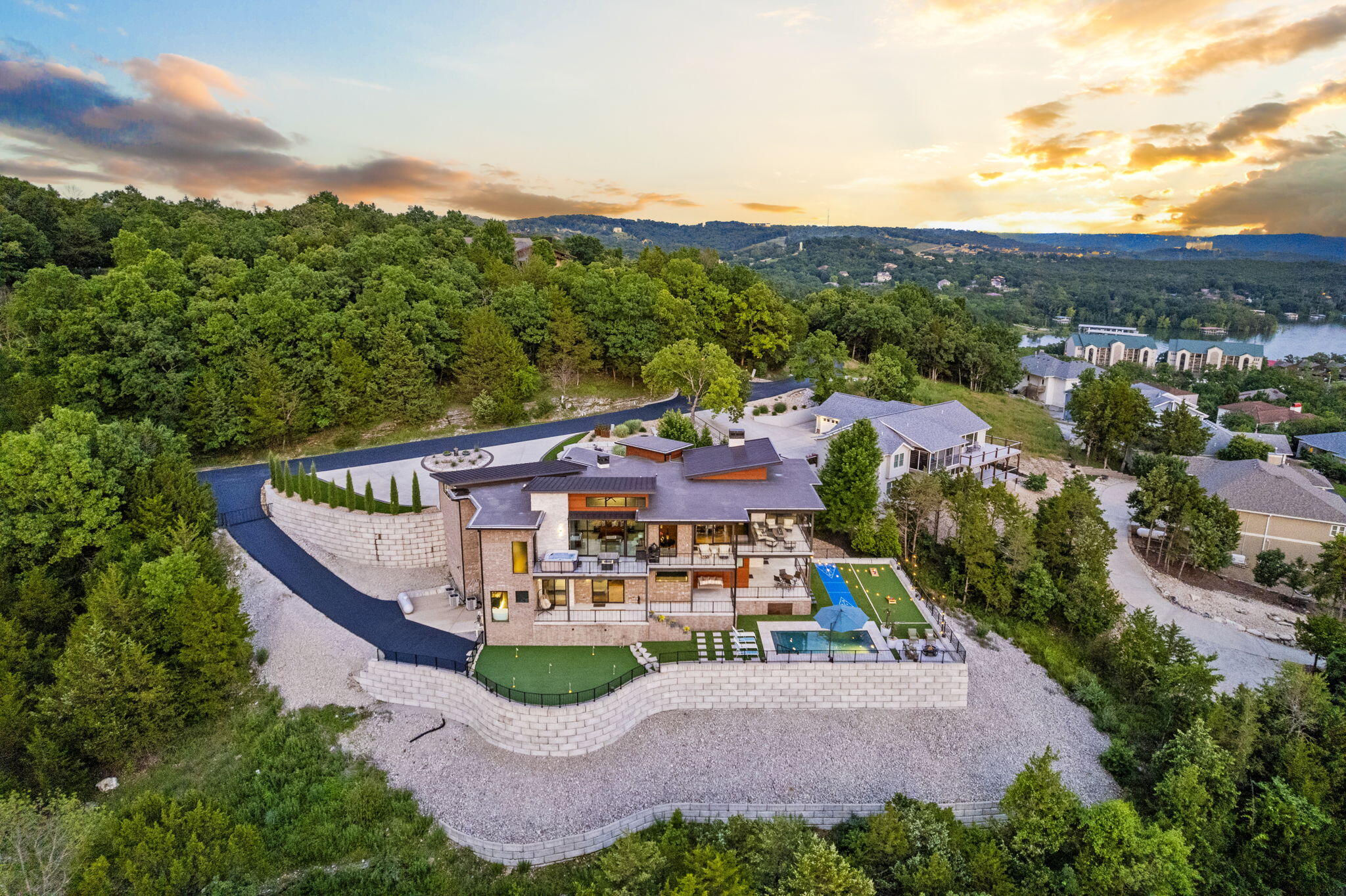 Experience unmatched luxury and breathtaking lake views at 355 Catalina, nestled in the exclusive gated community of Sunset Cove on Table Rock Lake. This exceptional home offers panoramic, unobstructed lake views from its elevated, private cul-de-sac location, with year-round sunsets enjoyed from expansive decks and a screened-in porch with hot tub access off the primary suite. Designed for low-maintenance living, the exterior features premium brick, stone, and metal siding, along with artificial turf, lush landscaping, and a circular driveway with a water feature. The sports field below includes a putting green with lighted cups, shuffleboard, bocce ball court, 12x24' gunite in-ground pool, fire pit, and an impressive sound system covering the entire outdoor space. Inside, the open-concept upper level boasts floor-to-ceiling retractable glass doors, a chef's kitchen with top-of-the-line Thermador appliances, a massive 5'x12' island, brushed Brazilian granite, and custom cabinetry. Additional highlights include a full bar, smart home sound system, central vac, pivot entry door, stone accent walls, and luxury finishes throughout. The primary suite is a retreat of its own with vaulted ceilings, lake views, motorized blinds, a spa-inspired bath with a custom tile shower and dual vanities, plus direct access to the hot tub for stargazing. Downstairs, enjoy a floating steel staircase, a second full bar, oversized en-suite guest rooms, built-in bunks, soaking tub, and laundry on both levels. Tech-ready and energy-efficient with Bosch HVAC, Kinetico water treatment, industrial ice maker, and dual water heaters. The oversized 3-car garage features epoxy flooring, utility sink, and extensive storage. Bonus: 10'x30' covered boat slip with lift available just 0.5 miles away.