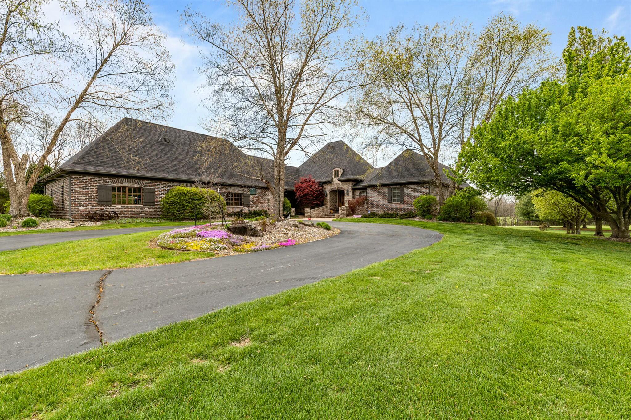 Tucked away on a beautifully secluded 7.5-acre lot in Rogersville, just minutes from Springfield, this custom-built estate offers nearly 7,000 square feet of thoughtfully designed living space. A long paved private drive leads you to the home, featuring four attached garage spaces and a fully insulated detached shop with electric, additional garage bays, and carport parking--perfect for storage, hobbies, or extra vehicles. Inside, you're welcomed by a spacious foyer, a formal dining room, and a versatile bonus space with access to the expansive back deck, ideal for entertaining. The main living area boasts beamed ceilings, a cozy corner fireplace, and opens into the kitchen and breakfast nook. The kitchen is warm and inviting with rich wood cabinetry, beautiful countertops, stainless steel appliances, and two oversized walk-in pantries for ultimate organization. Throughout the main-level you'll find stunning hardwood hickory plank flooring and travertine tile, adding both warmth and durability to the home. The main-level primary suite is generously sized with a spa-like ensuite featuring a soaking tub, large walk-in shower, dual vanities, and a spacious walk-in closet. Also on the main level, you'll find a dedicated office, utility room, three guest bedrooms, and two full bathrooms. Downstairs, enjoy a second living area with a wet bar and fireplace, two additional guest bedrooms--one of which could serve as a second primary suite with its own large full bath--and an additional half bath with utility access. Step outside to your own private oasis with an in-ground saltwater pool, a huge yard for play or relaxation, and stunning panoramic views. This one-of-a-kind property offers the perfect blend of privacy, space, and convenience.