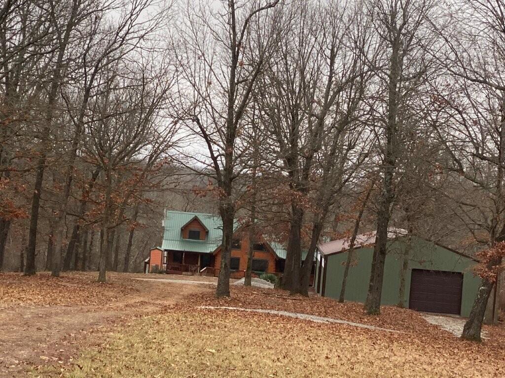 Discover your own piece of paradise in this charming log cabin nestled on 80 acres within the serene Ozark Mountains of SW Missouri yet close to NWA. Behind the gated entrance you'll find an expansive property with beautiful mature trees, four ponds, and rolling pastures seeded with rye and fescue in 2024. Built in 2015, the cabin boasts rustic charm with its classic log construction. Once inside, your attention is immediately drawn to quality Amish craftsmanship and the magnificent floor-to-ceiling stone backdrop for the wood stove. The living area exudes warmth and comfort, featuring exposed beams that add character and charm. The large windows allow natural light to immerse the living space and provide picturesque views. The new shop built in 2024 is 40x60x11 and has two 10' automatic garage doors, electricity, and clean concrete floors. This beautiful home and unrestricted land provide the perfect blend of privacy, natural beauty, and a peaceful atmosphere away from the hustle and bustle.