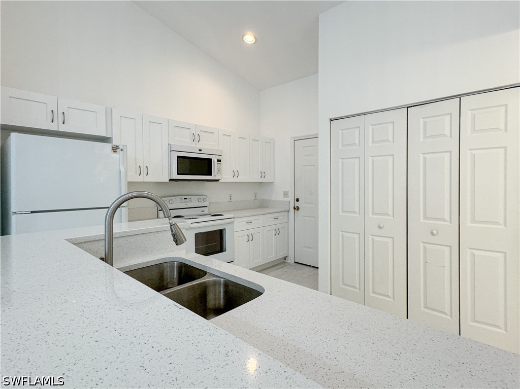 Kitchen with white cabinetry, sink, light stone co