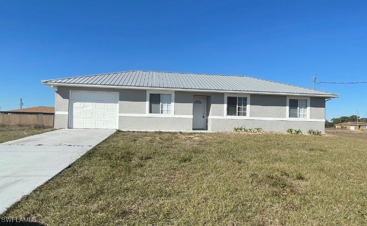 Ranch-style home featuring metal roof, a front lawn, and stucco siding