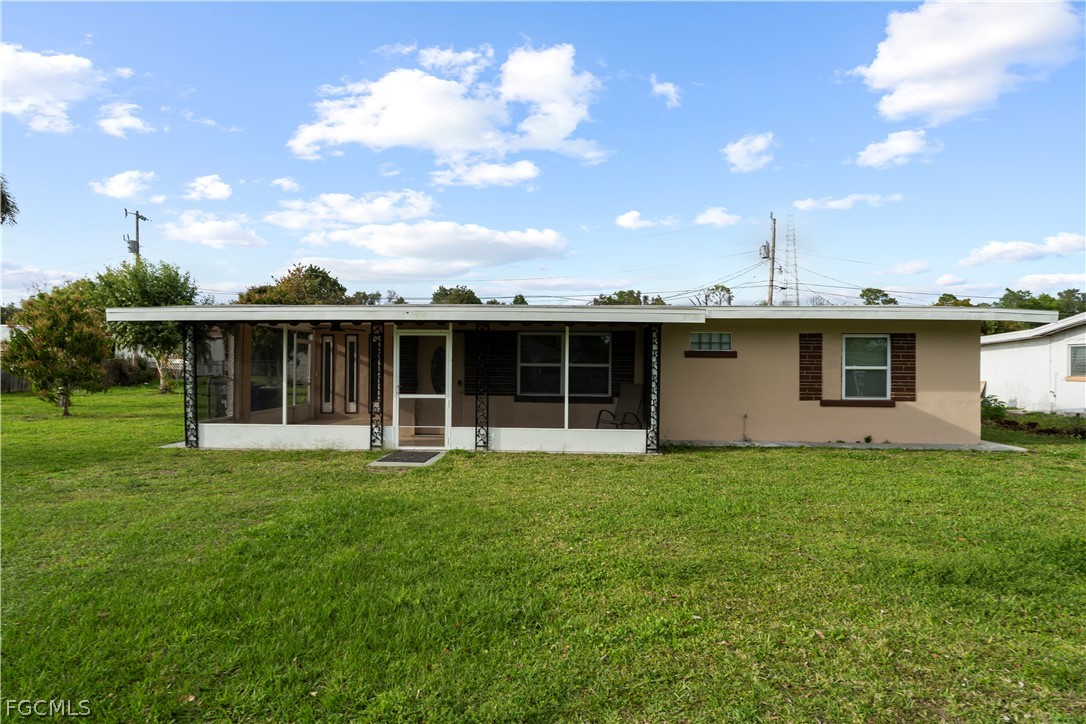 Front of property with a sunroom, a lawn, and stuc