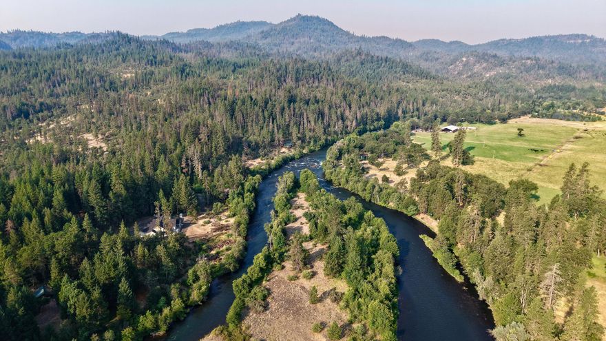 Premier Upper Rogue Riverfront home with 300 ft. of frontage, stunning river views and an island across the way. Nestled on 11.5-acres, this 2,979 sq. ft. Adair Tamarack plan offers 3 beds, 3 baths, an open-concept layout, vaulted ceilings, river rock fireplace, chef's kitchen with island & pantry, tile floors with radiant heat, and a luxurious primary suite with soaking tub. Enjoy the covered front porch and river-facing deck with pine ceiling. Finished 3-car garage, 30-amp RV hookup, water filtration and 19 GPM shared well. Gated entry, paved road, and access to 160 recreational acres shared with 4 properties, bordering vast, limited-access BLM land—an outdoor enthusiast's dream!