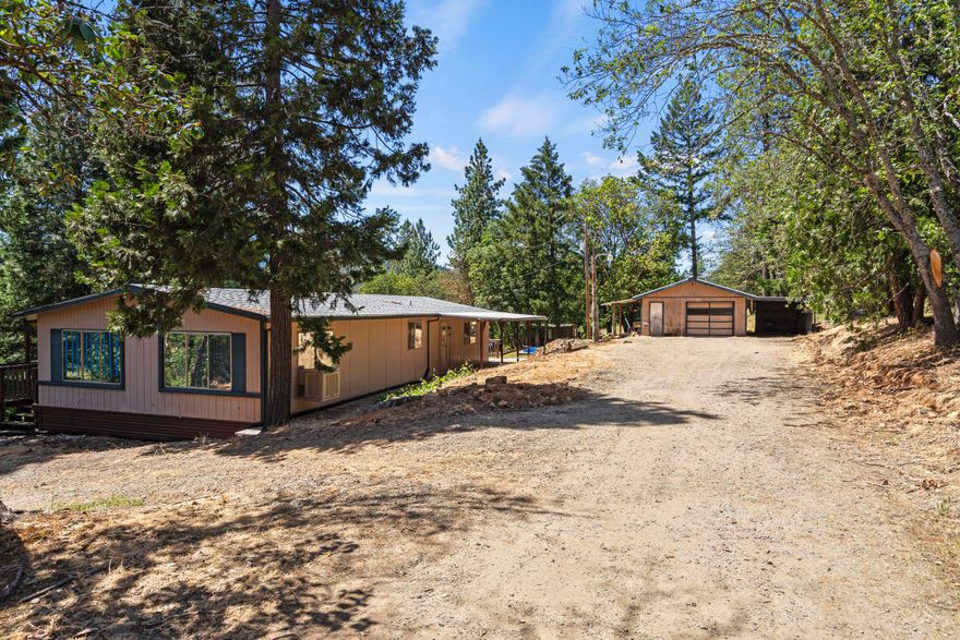 Private haven on 4.98 wooded acres! Charming home w/ breathtaking valley & mountain views, providing peaceful retreat. Living room, w/ numerous windows & built-in cabinets, invites natural light. Kitchen w/ ample cupboard space, a pantry, & eat bar, flowing into adjacent dining room w/ cozy wood-burning stove & sliding doors that open to covered deck—perfect for indoor-outdoor entertaining. Primary bedroom w/ private bath. 2nd bedroom & full bathroom provide comfort for family or guests. Laundry room, w/ sink, built-ins, & exterior door, doubles as mudroom, ideal for country living. Step outside to gated, secure property w/ RV parking. The expansive deck wraps around the home, offering space to soak in surroundings. Detached garage w/ attached carport provides storage & workspace. Property is gardener's dream w/ space for favorite plants. Enjoy watching local wildlife in your private sanctuary, just 20 minutes from restaurants, shopping, and the Applegate River Golf Club.