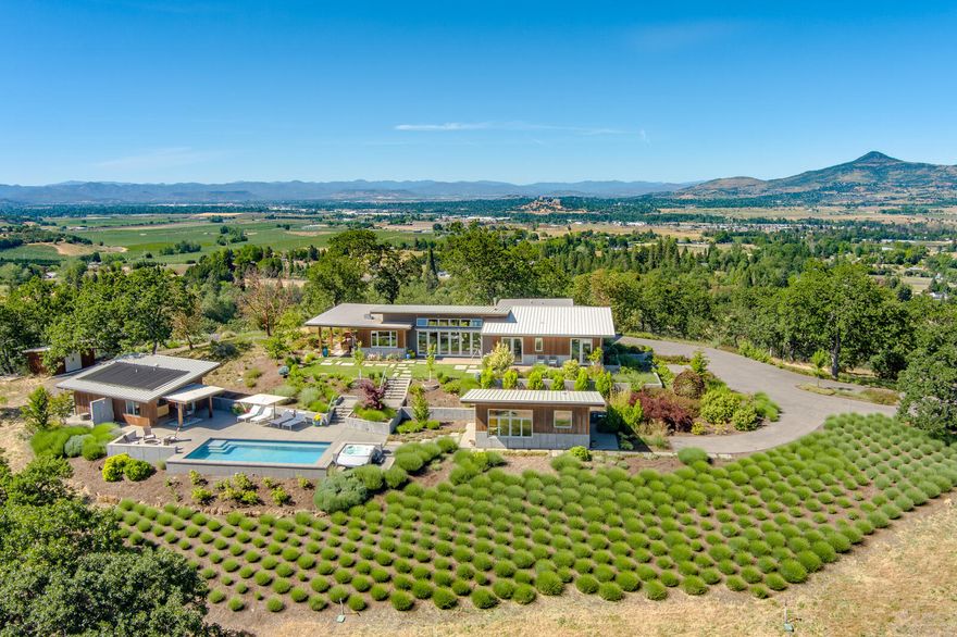 Have you ever been to a home that was so incredible you wanted to stay forever? That is how you will feel when you view this Knoll top paradise located just a few minutes outside Talent. Set down a quiet drive to provide privacy w/ views in every direction, this stunning property graced the cover of Oregon Home. The owners worked w/ local architects to build a sustainable home w/ active & passive solar, smart irrigation, & room to garden & play outdoors. The result is a single level contemporary custom home completed in 2017. The great room has 20-foot-wide folding doors on both sides to open the home to the outdoors. The property features two detached guest suites, each w/ its own full bath & kitchenette, a swimming pool, hot tub, & a pool house w/ laundry, kitchenette & outdoor shower. The home has extensive outdoor patio areas, 2 w/ gas fire pits surrounded by mature landscaping & an outdoor dining area. There is also a barn w/ a 300 sf workout room, a shop, & several outbuildings.